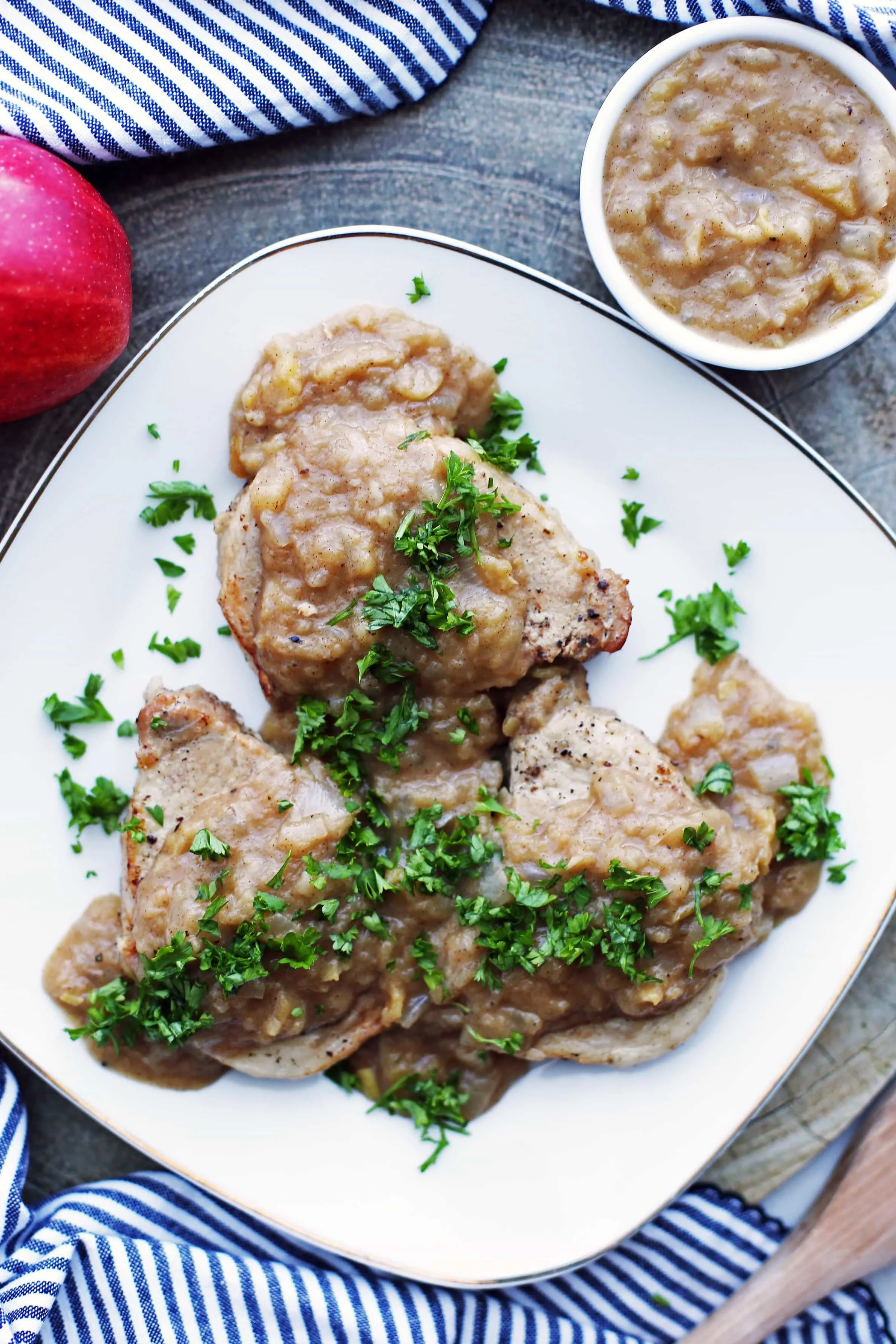 Three Instant Pot Pork Chops smothered with onion-apple sauce on a white plate with more sauce in a small white bowl beside the plate.