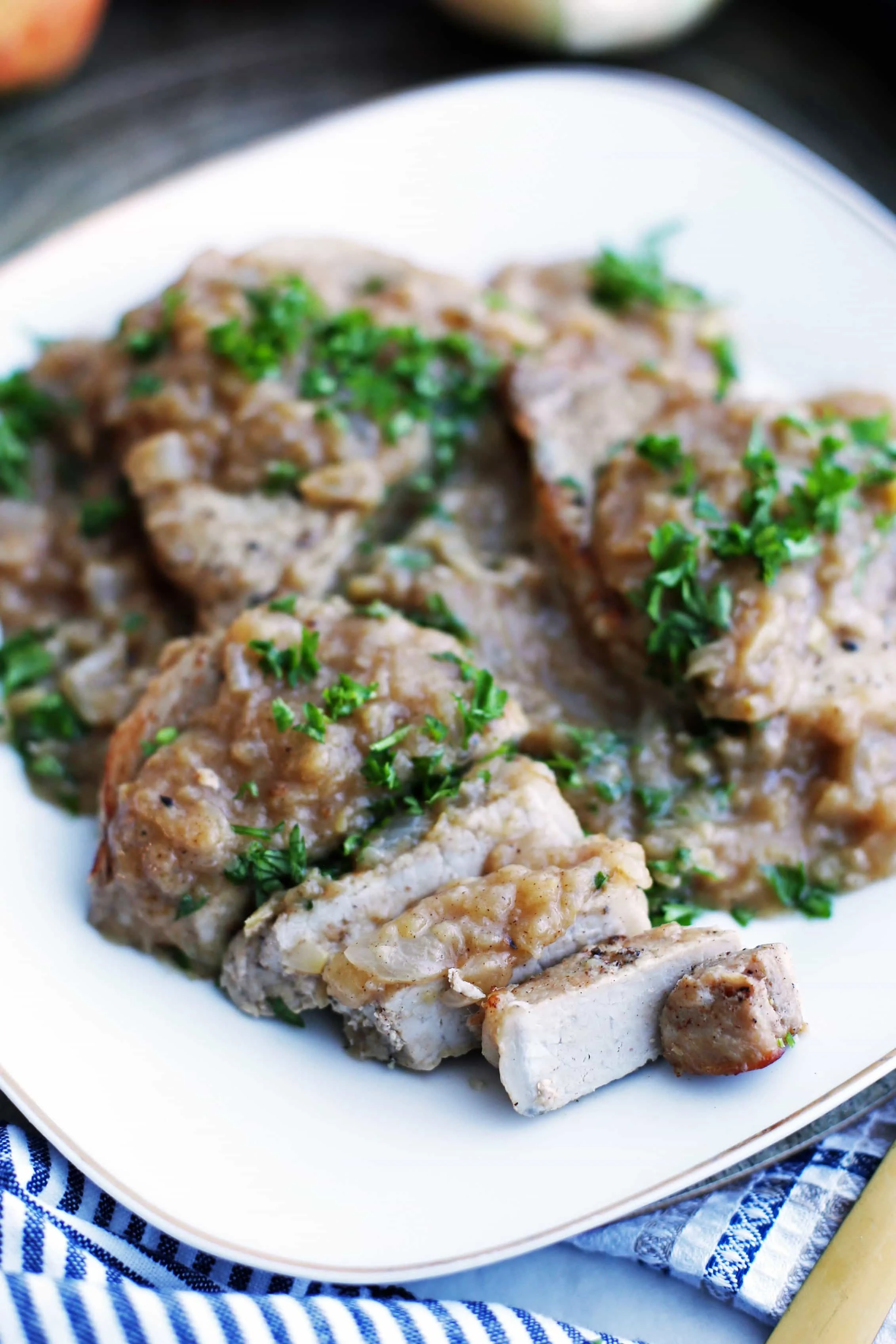 A closeup view of a boneless pork chop covered with onion-apple sauce sliced on a white plate.