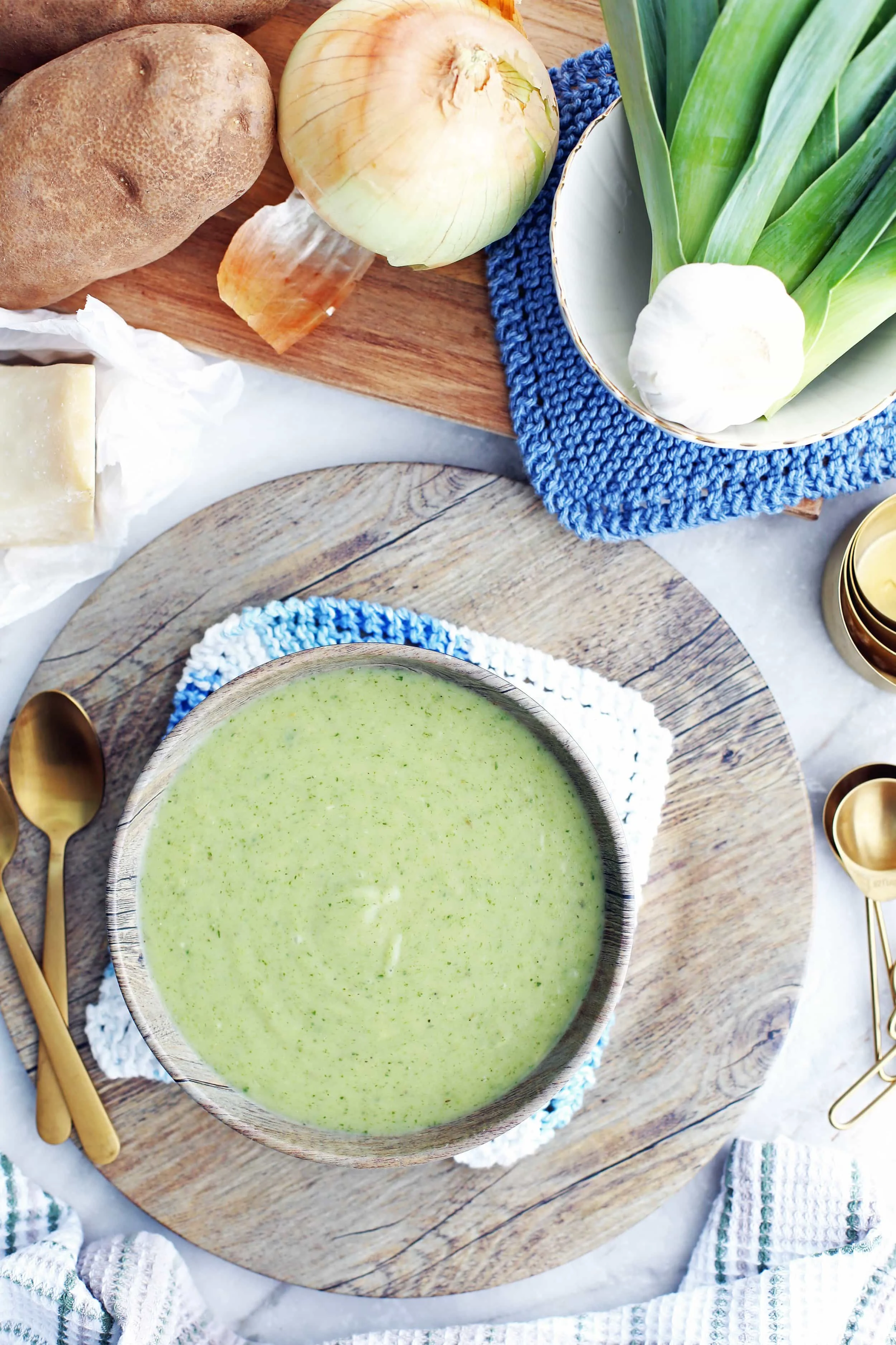 Overhead view of creamy Potato Leek Soup with Spinach and Parmesan in a bowl that's surrounded by fresh vegetables.