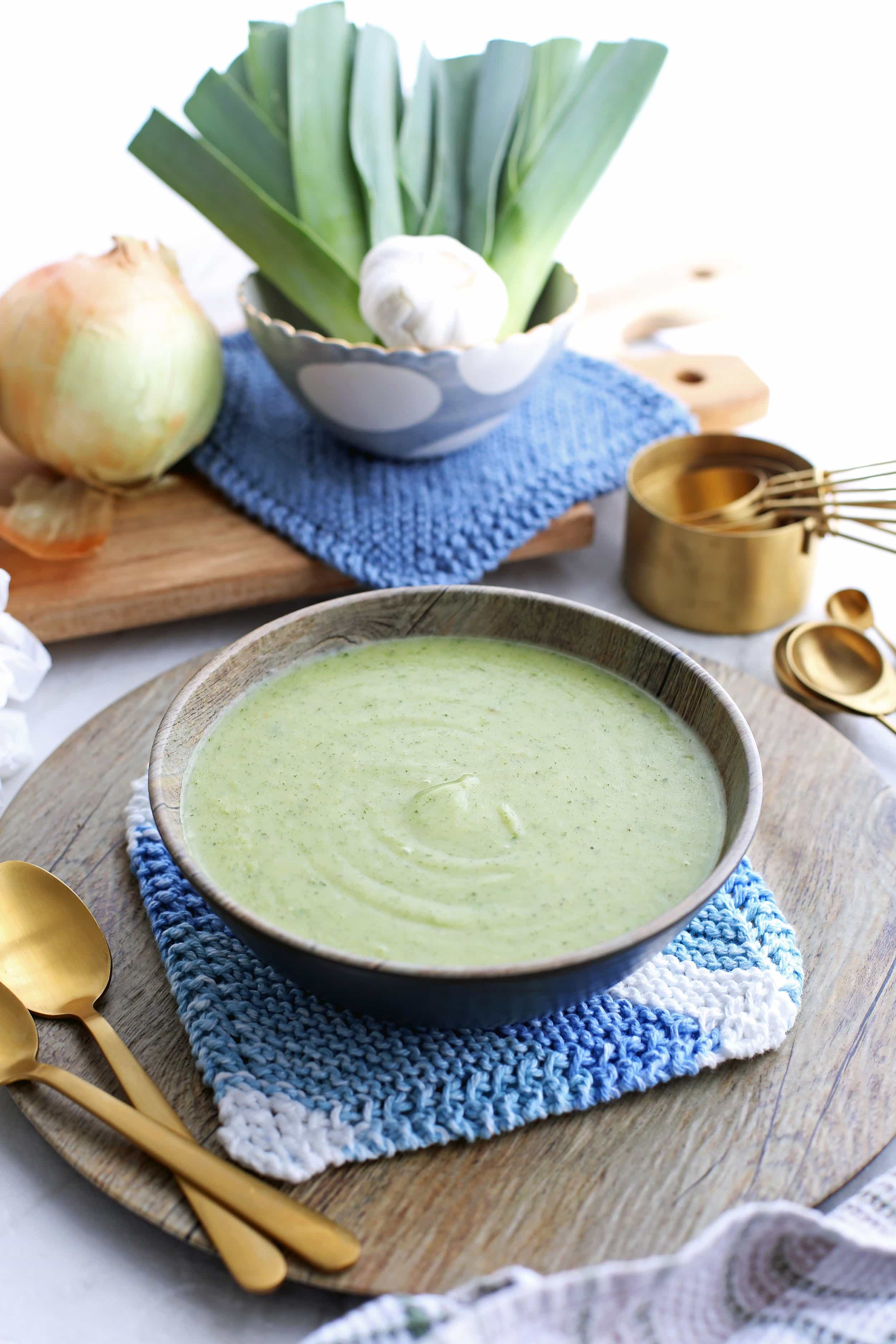 A bowl of creamy Potato Leek Soup with Spinach and Parmesan in a wooden bowl with spoons on the side.