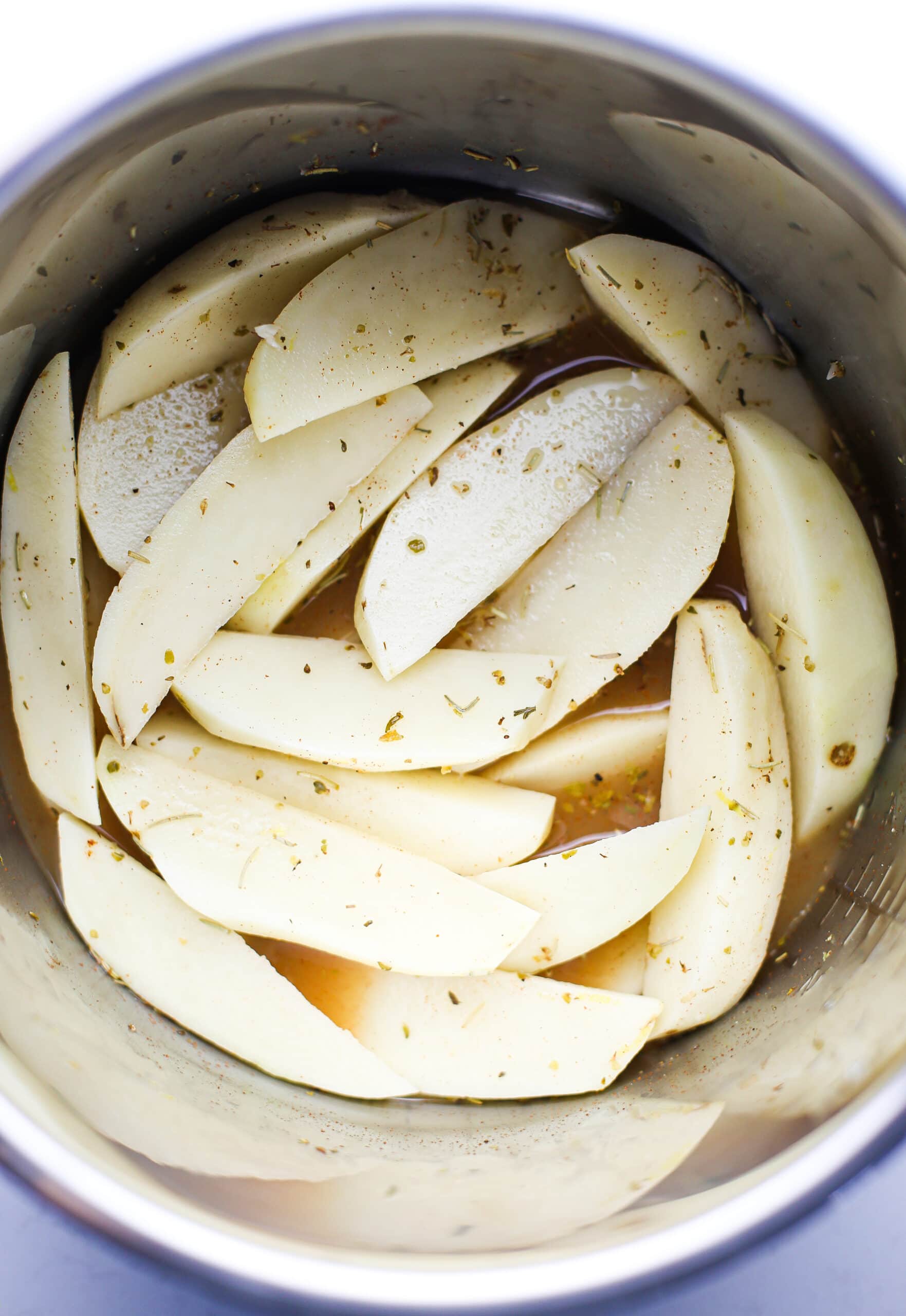 Overhead view of peeled and wedged potatoes in a herbed lemon chicken broth in the Instant Pot.