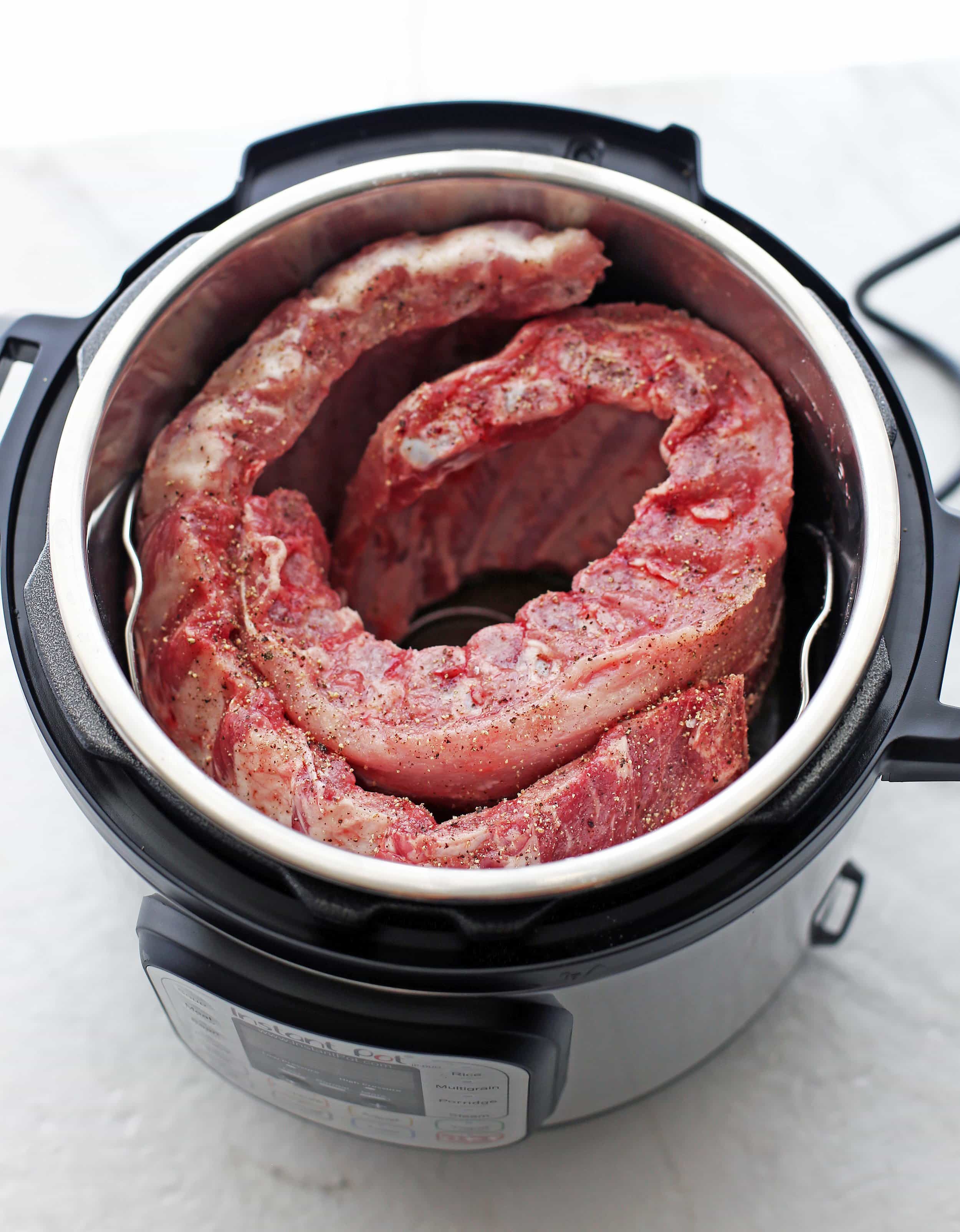 Two raw rack of pork ribs curled around the inside of an Instant Pot.