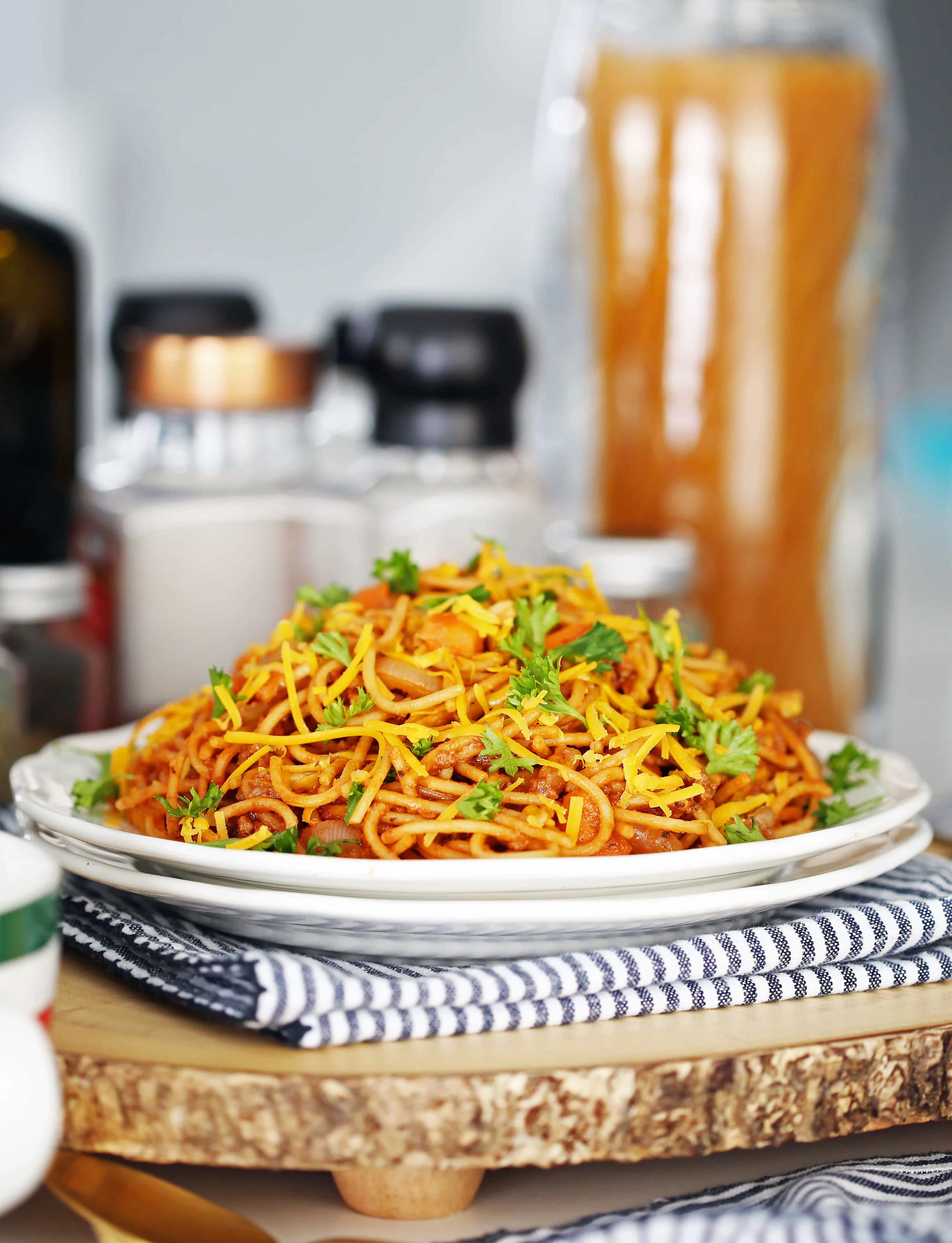 A side view of spaghetti and meat sauce with parsley and cheese on a white plate.