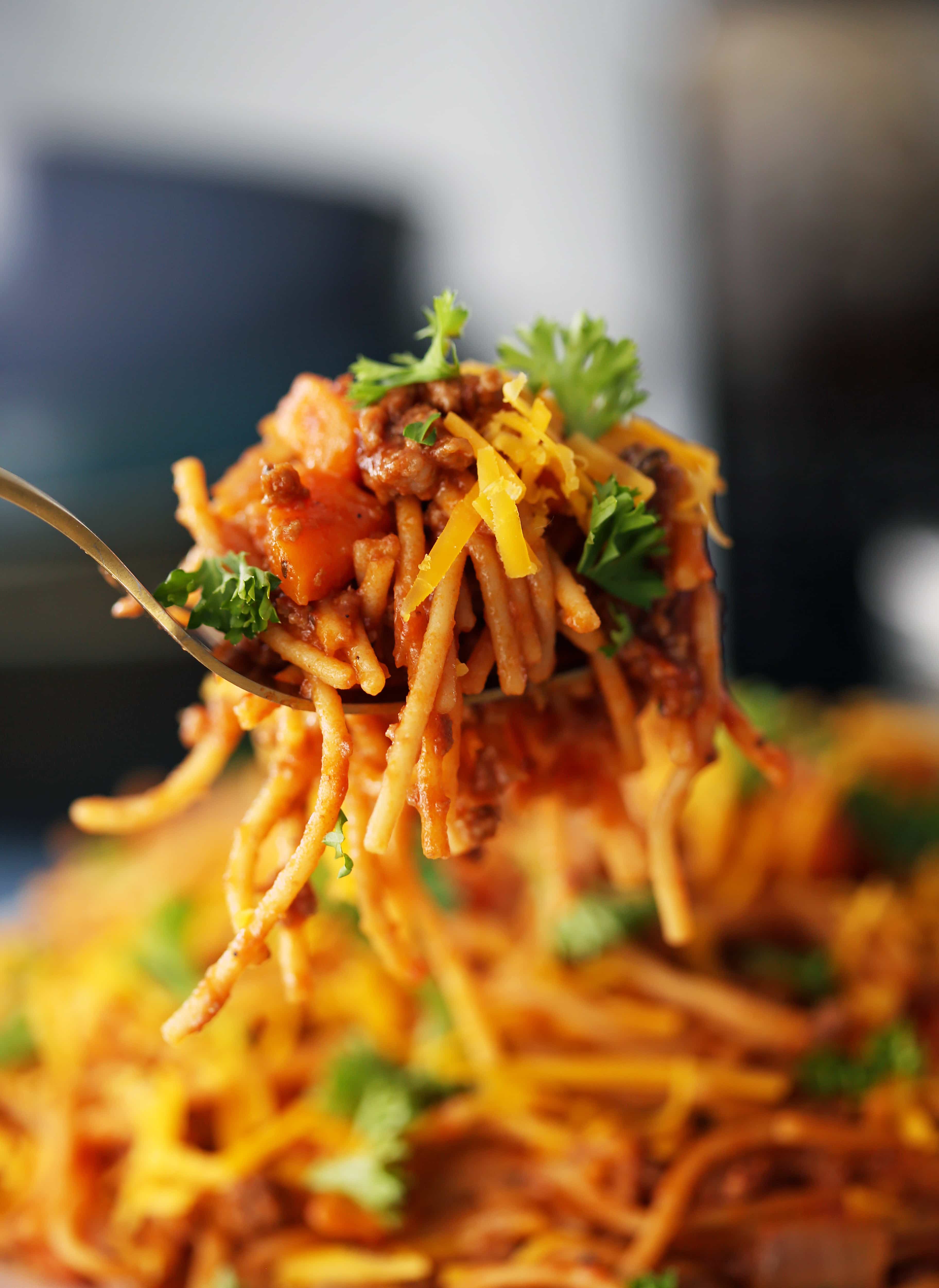 A closeup view of a fork holding Instant Pot spaghetti and meat sauce with cheese and parsley.