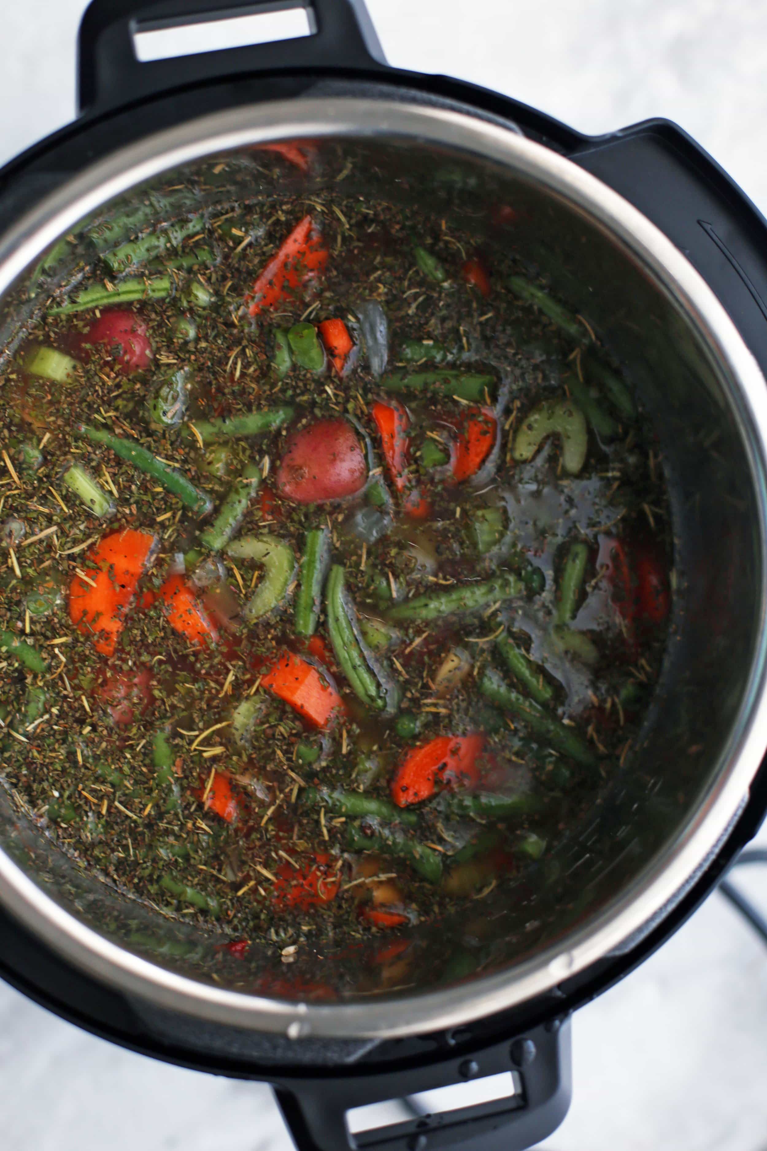 Raw vegetables, dry brown rice, and vegetable broth in the Instant Pot.