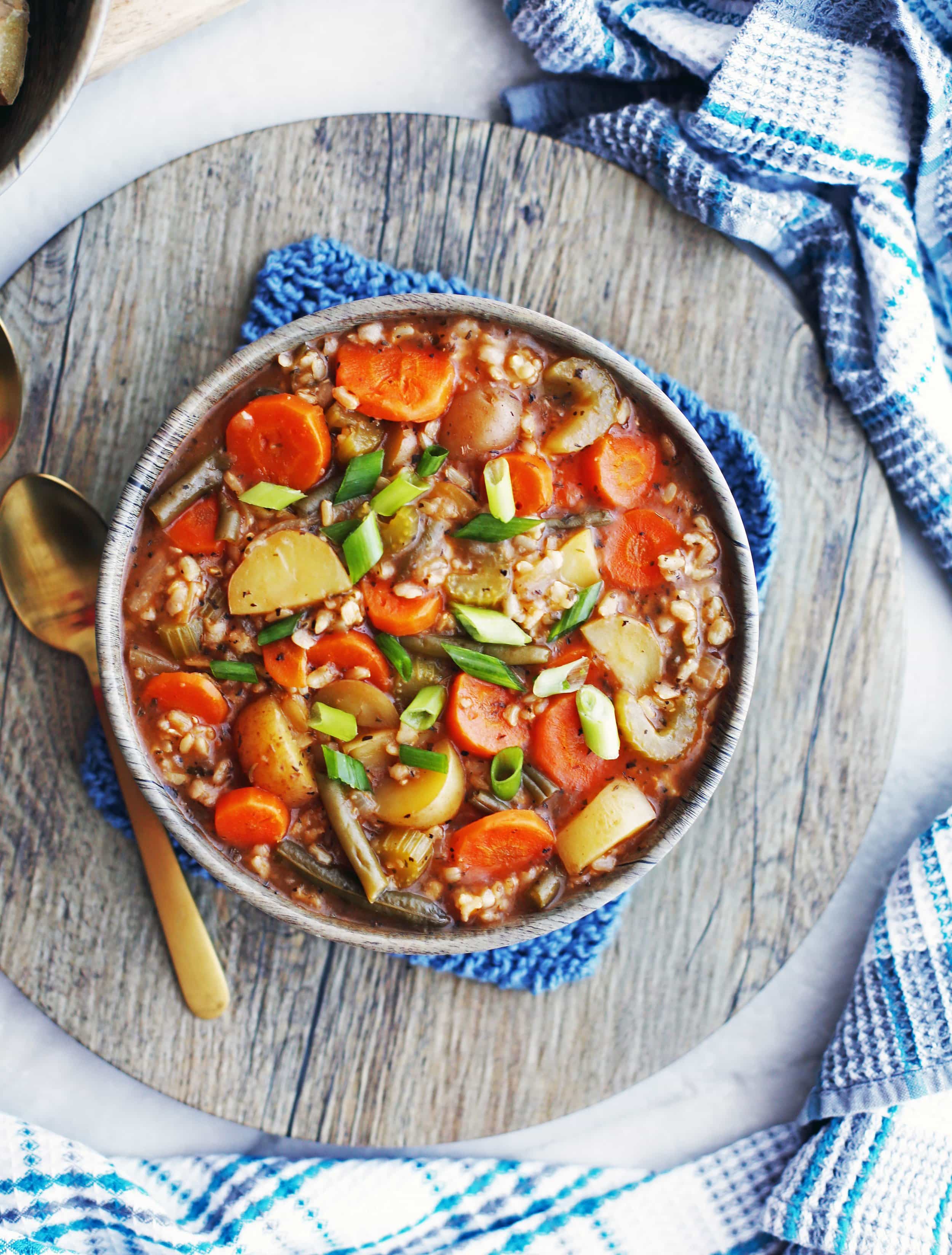 An overhead shot of a bowl of vegetable and brown rice soup with green onion garnish.