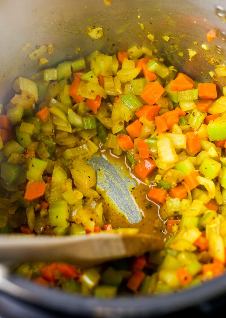 Closeup of spiced diced vegetables and a wooden spoon in the Instant Pot.