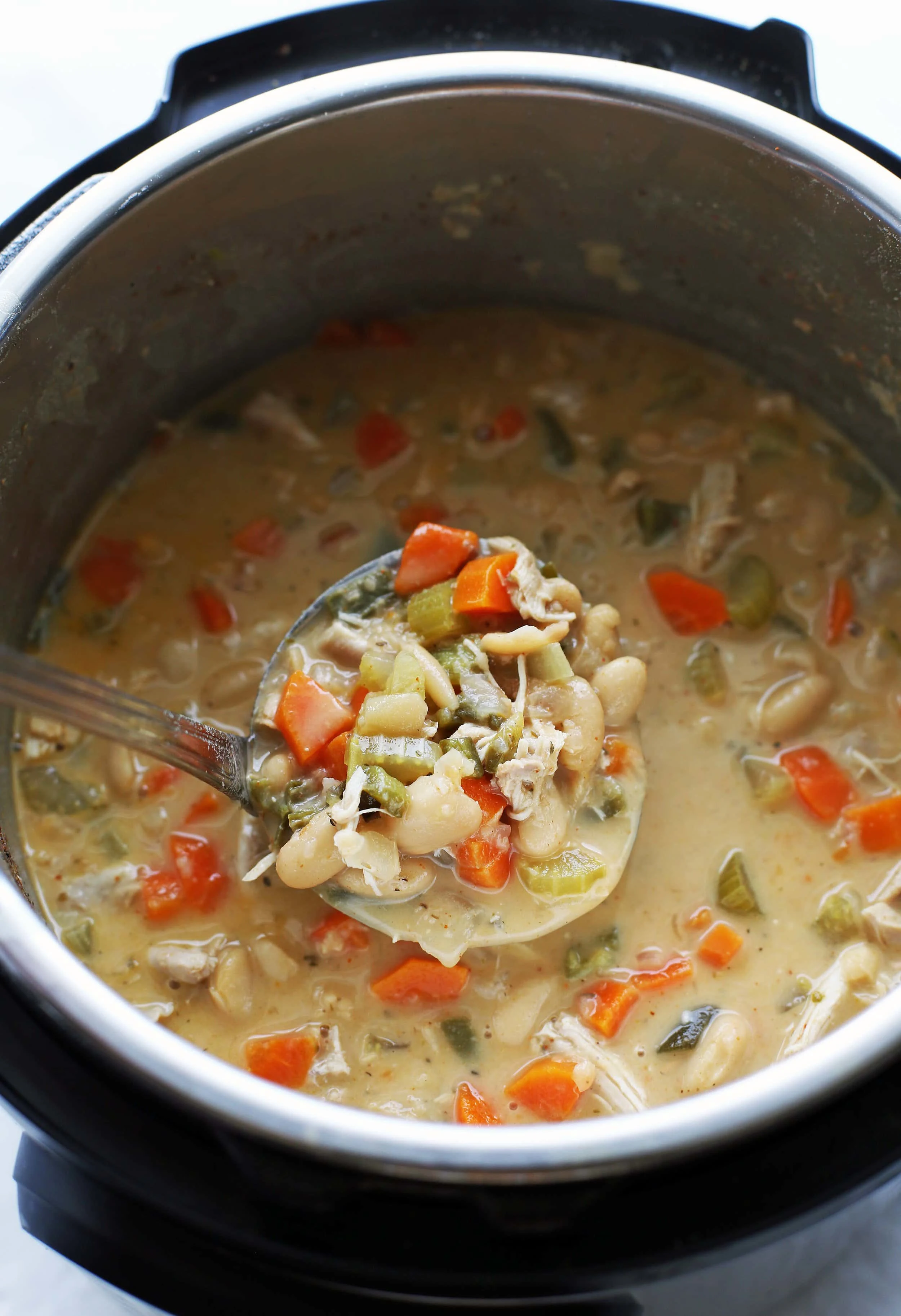 A large metal ladle holding a big scoop of White Bean Chicken Chili above more chili in the Instant Pot.