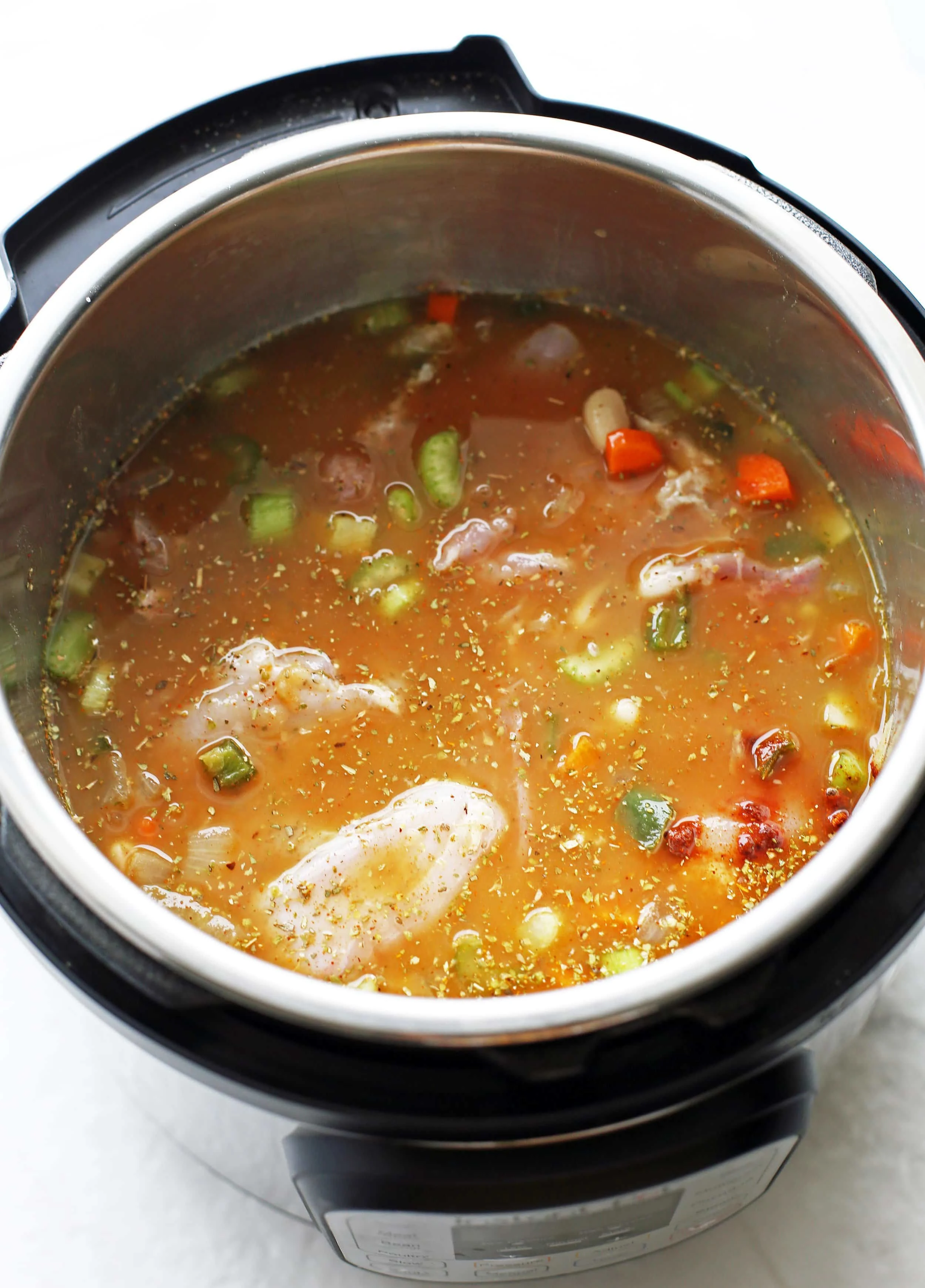 Diced vegetables, spices, raw chicken thighs, and chicken broth in the Instant Pot.