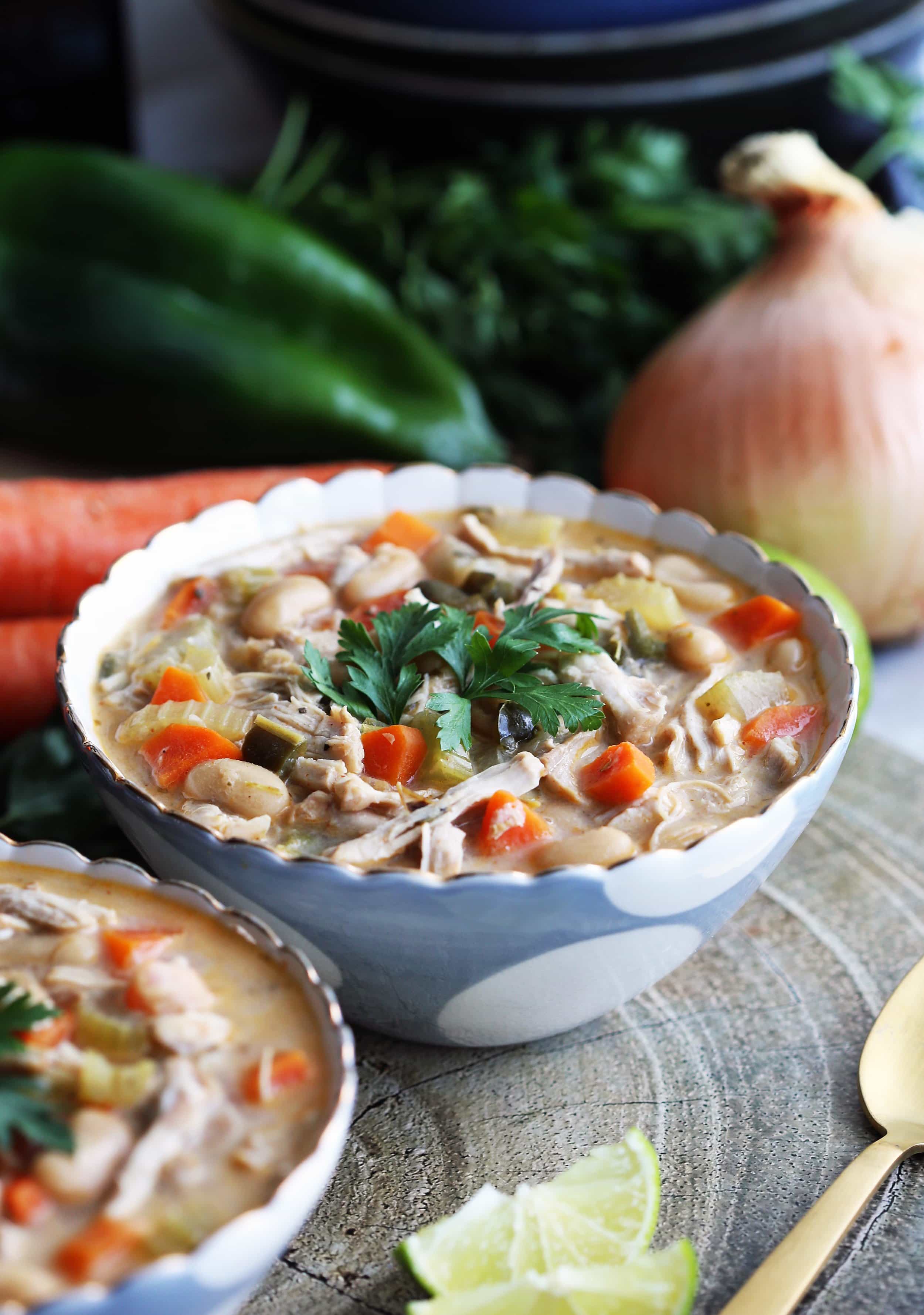 A blue bowl containing Instant Pot White Bean Chicken Chili with fresh vegetables in the background.