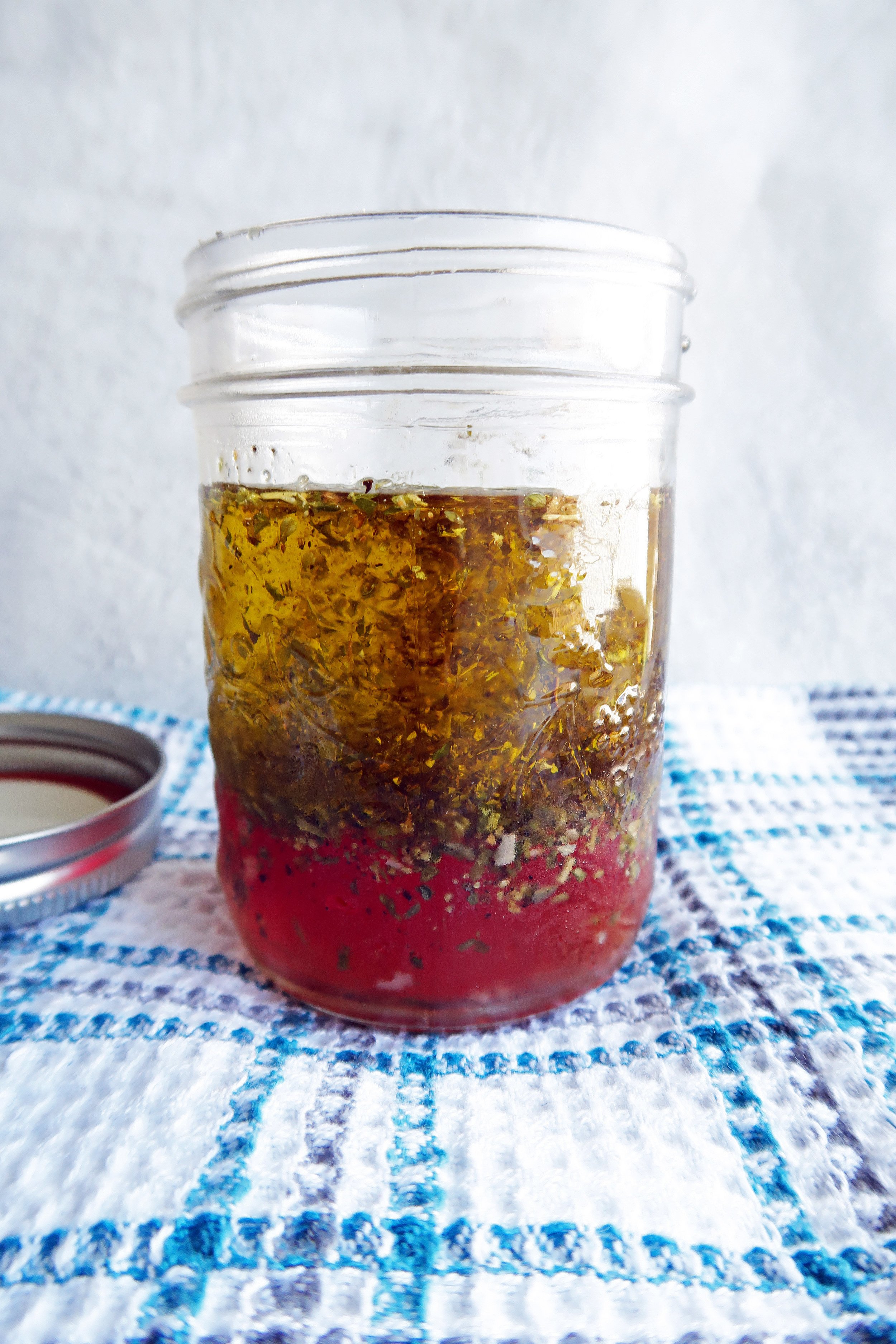 A jar of Italian vinaigrette ingredients that has not been whisked.