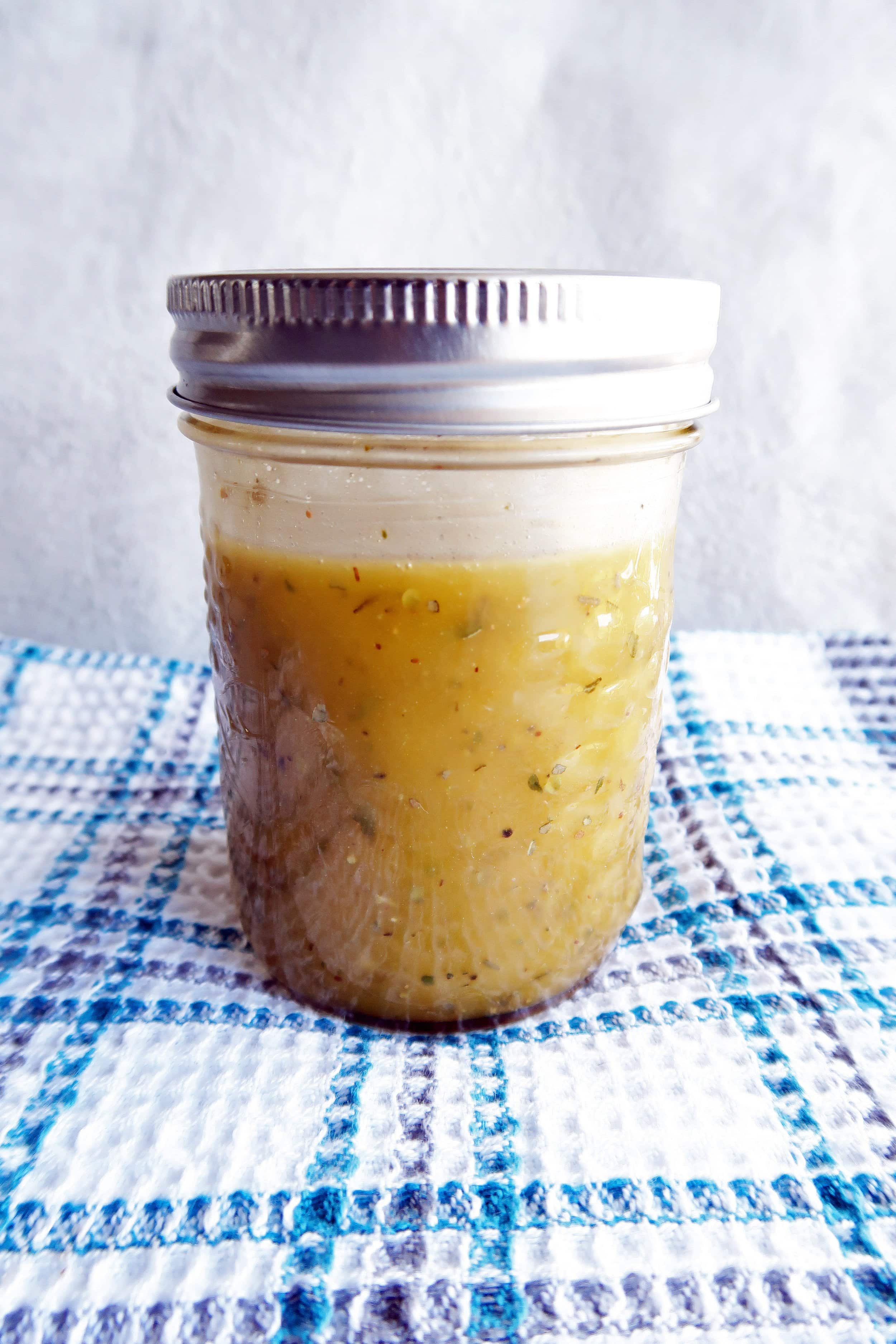 A jar of Italian vinaigrette which includes olive oil, red wine vinegar, garlic, honey, and herbs.