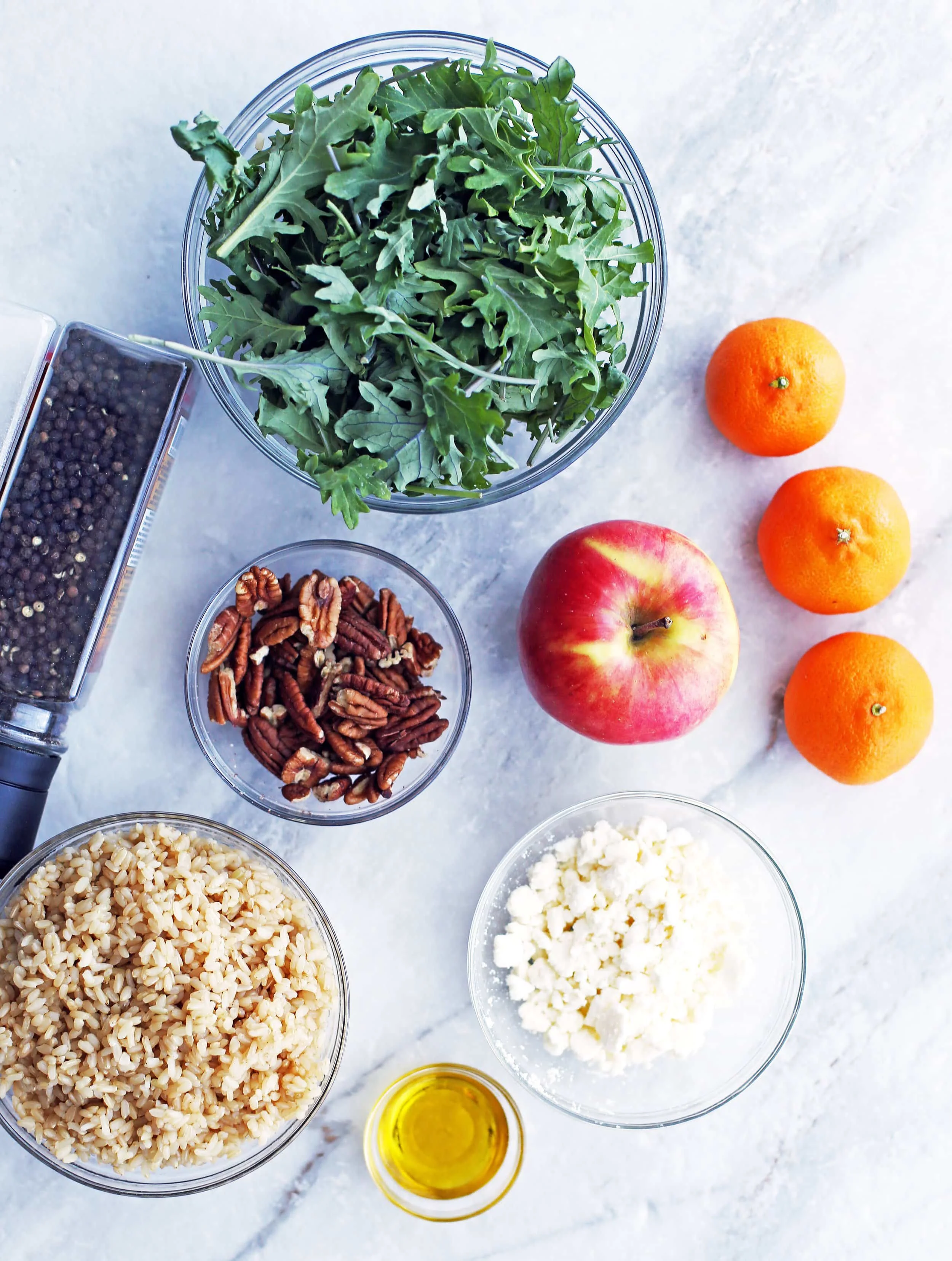 Bowls of baby kale, brown rice, pecans, feta, olive oil, and an apple, clementines, and salt and pepper.