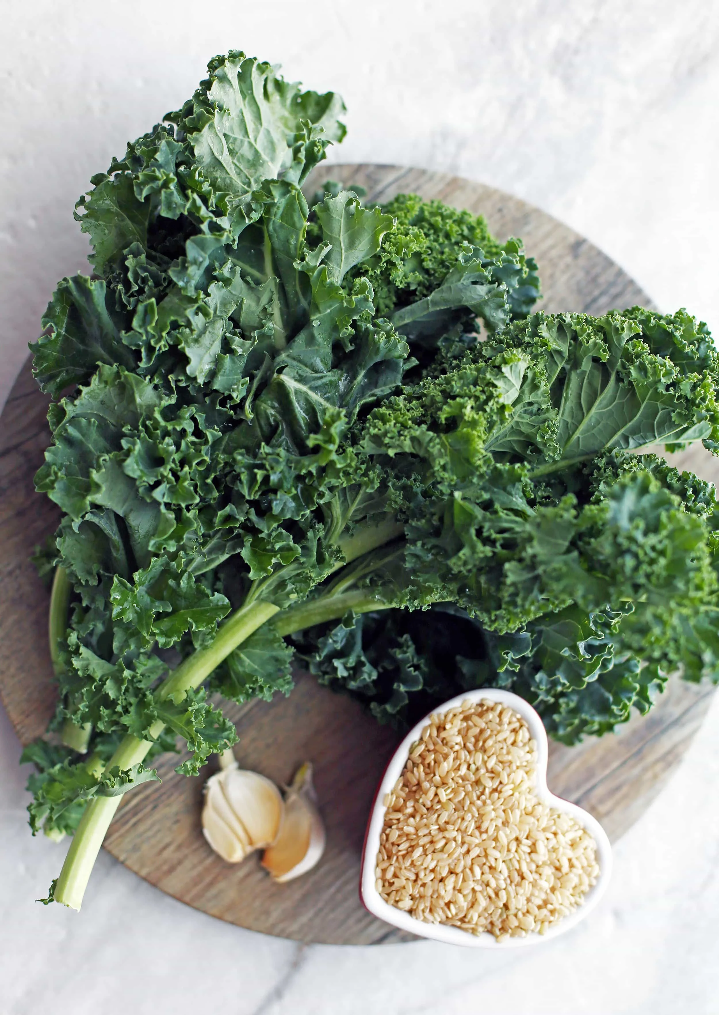 Overhead view of fresh green kale, garlic cloves, and a small bowl of brown rice.