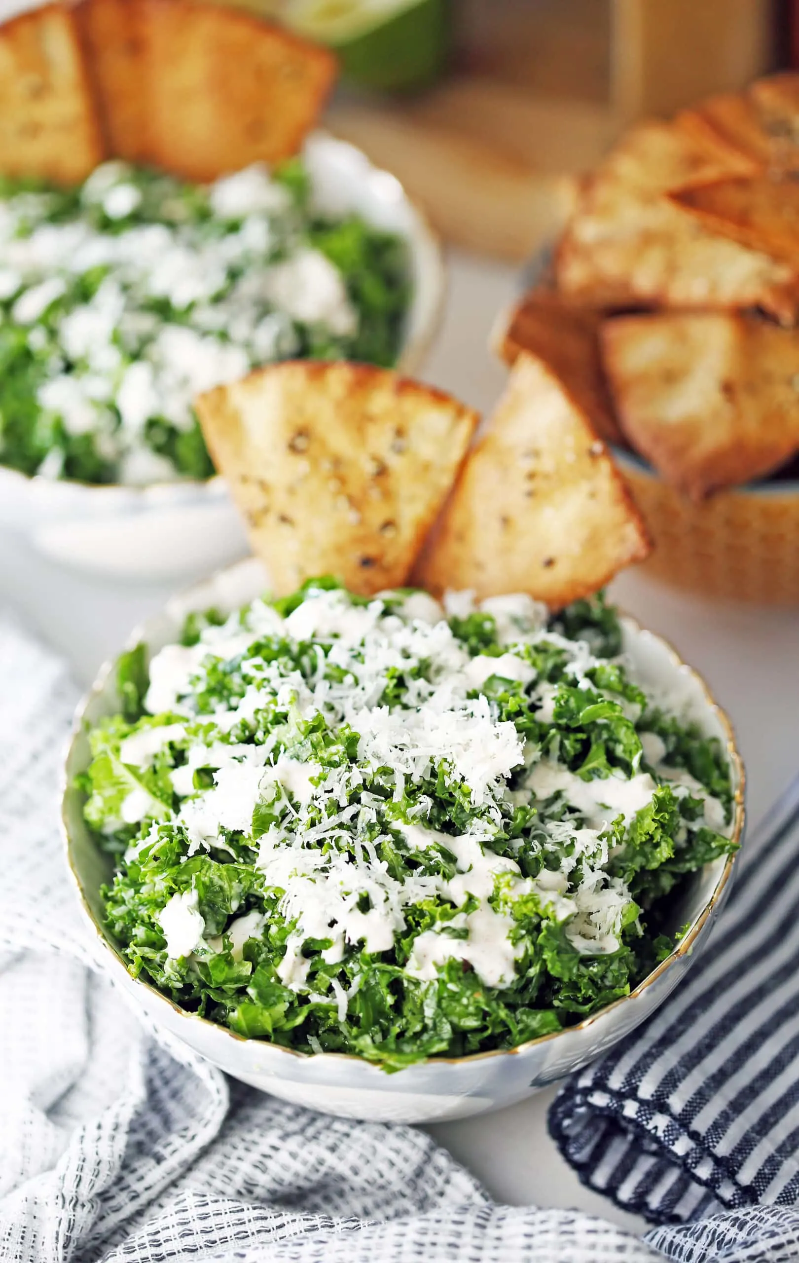 A bowl full of kale salad with parmesan, garlic lime dressing, and pita chips.