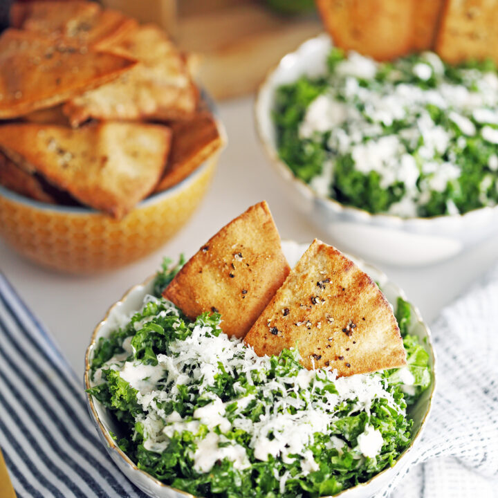 Kale parmesan salad with yogurt dressing and pita chips in two bowls and another bowl full of pita chips.