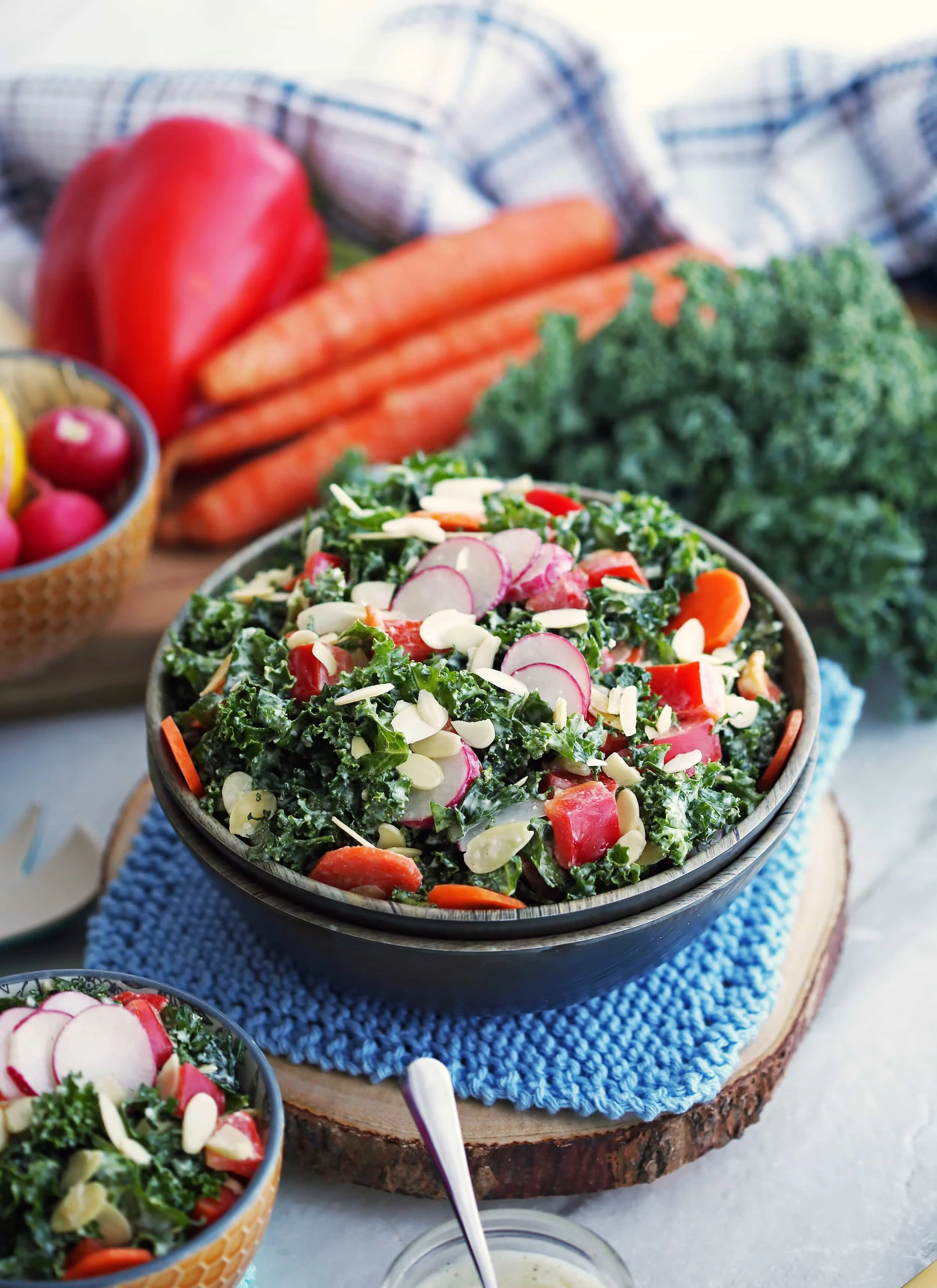 Crunchy salad made with kale, carrots, radishes, peppers, almonds, and parmesan yogurt dressing in a wooden bowl.
