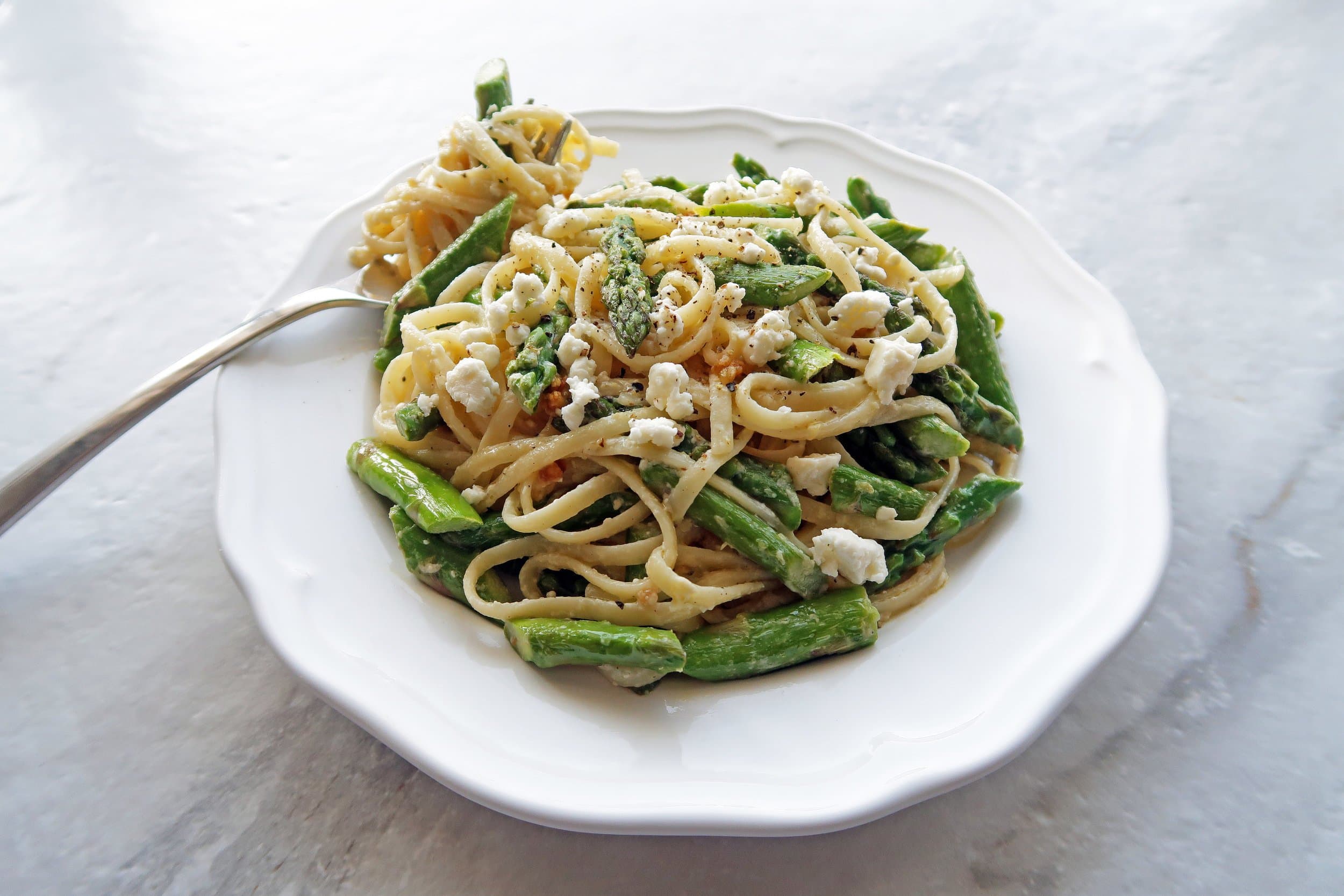 Lemon Feta Linguine with Garlic Asparagus on a white plate with linguine twirled around a fork.