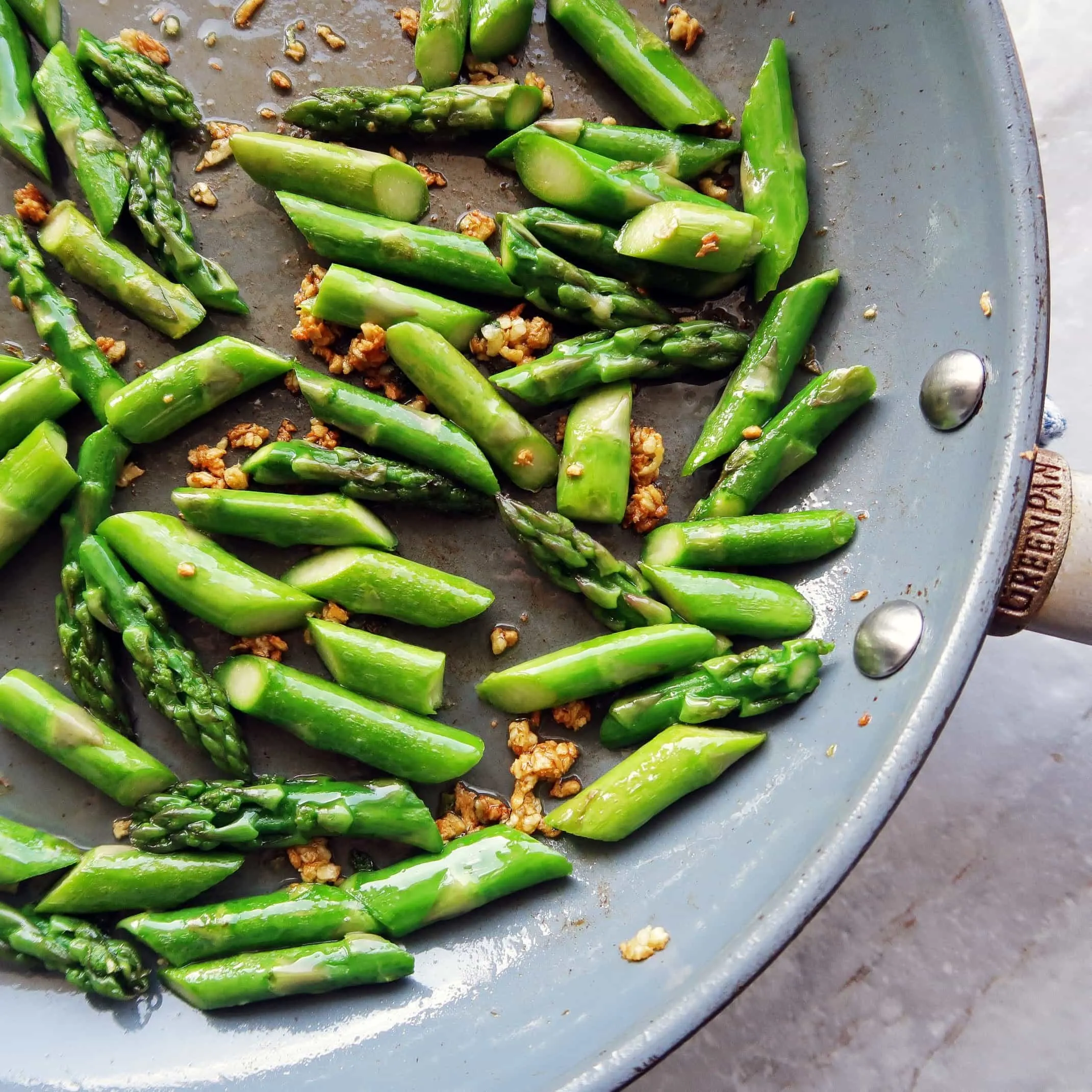 A saute pan featuring sliced asparagus and crispy brown garlic.