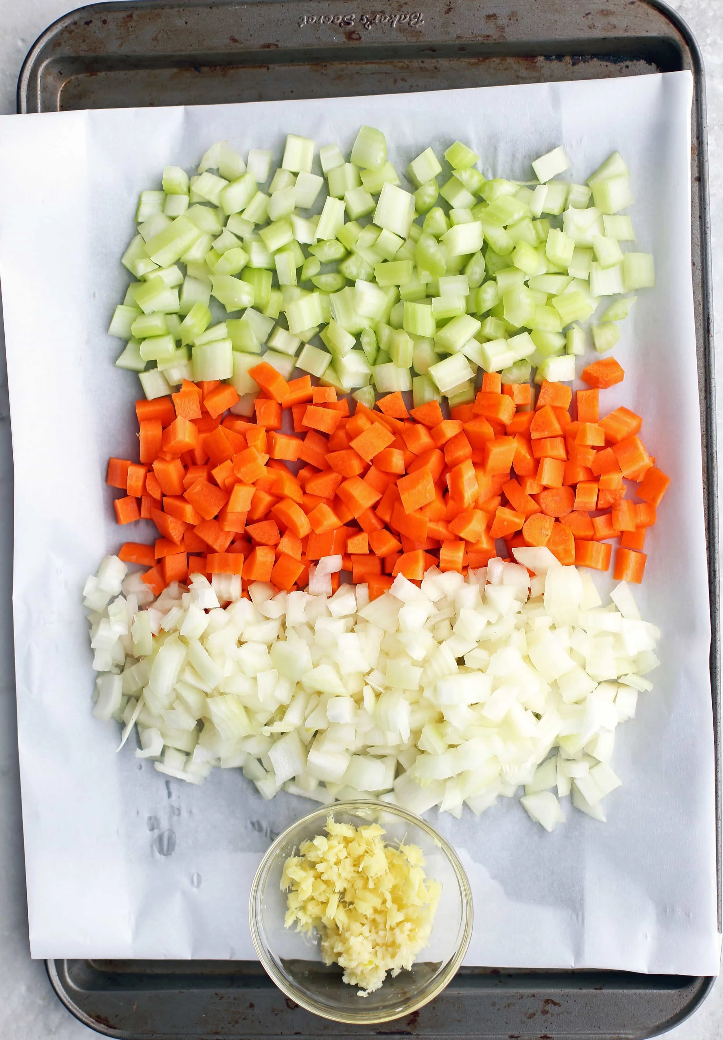 Diced onions, carrots, and celery in a baking sheet; minced garlic and ginger in a small bowl.