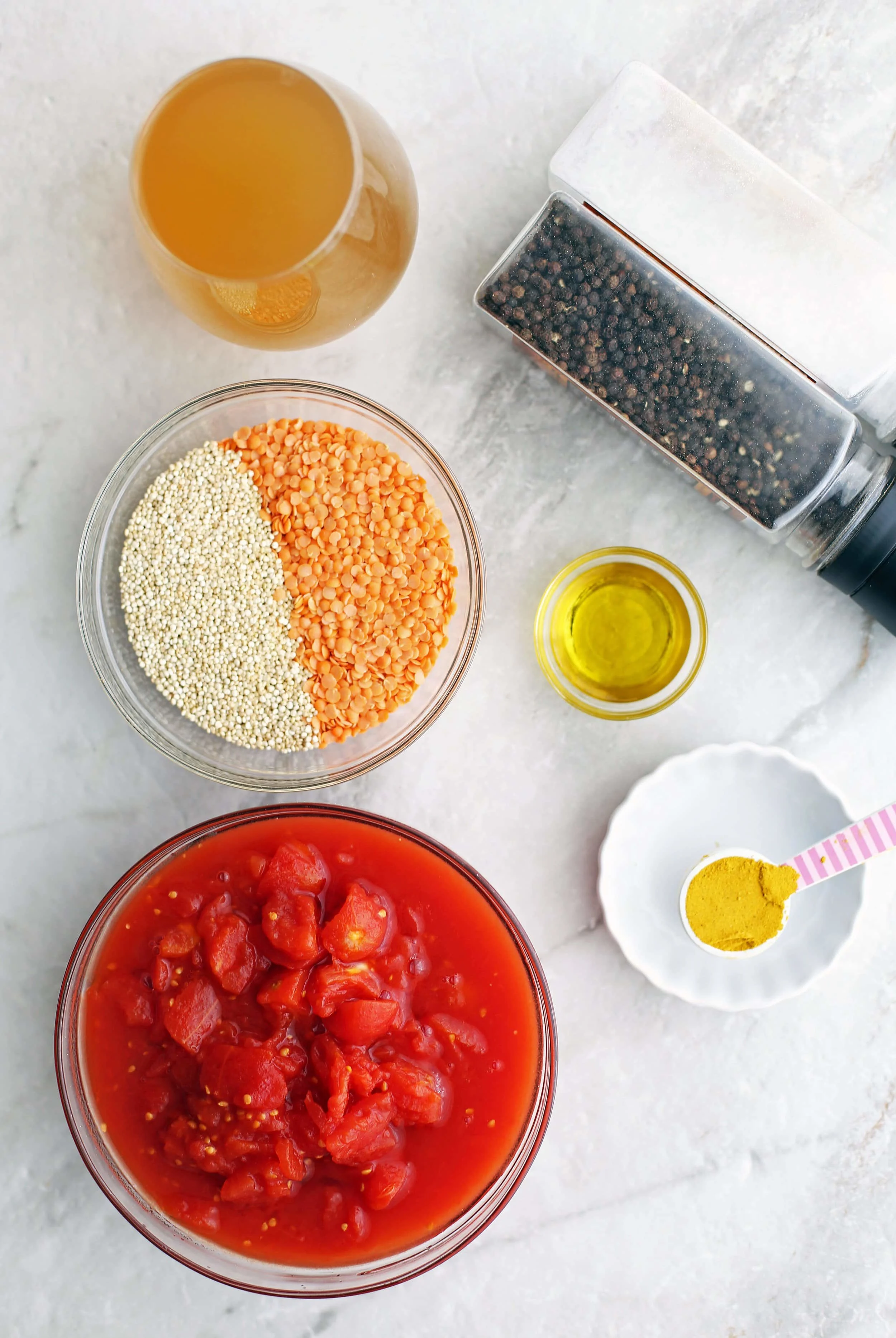 Bowls of diced tomatoes, quinoa, red lentils, vegetable broth, curry powder, olive oil, and salt and pepper shakers.