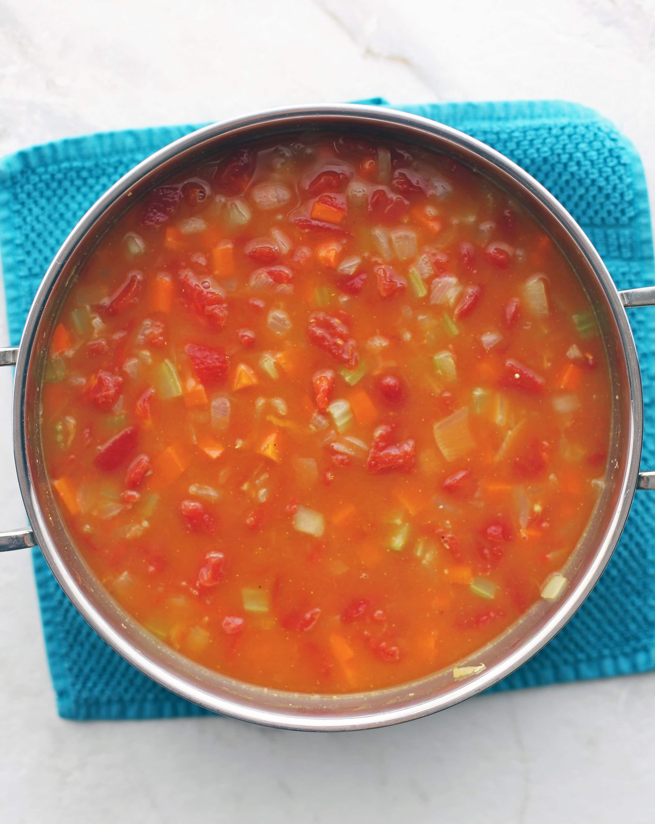 A big pot full of vegetables, dry lentils, dry quinoa, and vegetable broth that ready to be cooked.