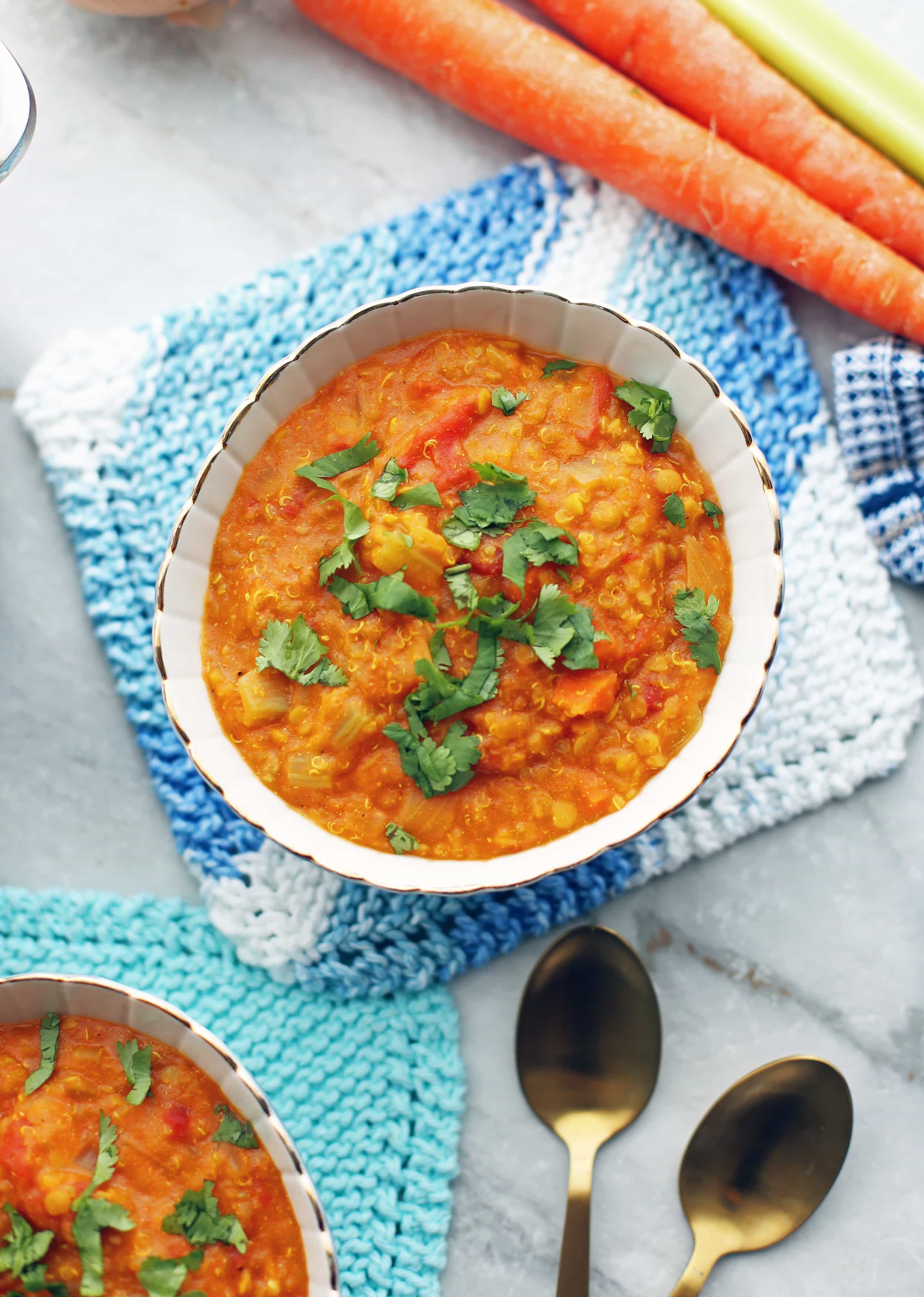 Overhead view of Curried Red Lentil and Quinoa Vegetable Soup in a small bowl with spoons beside it.