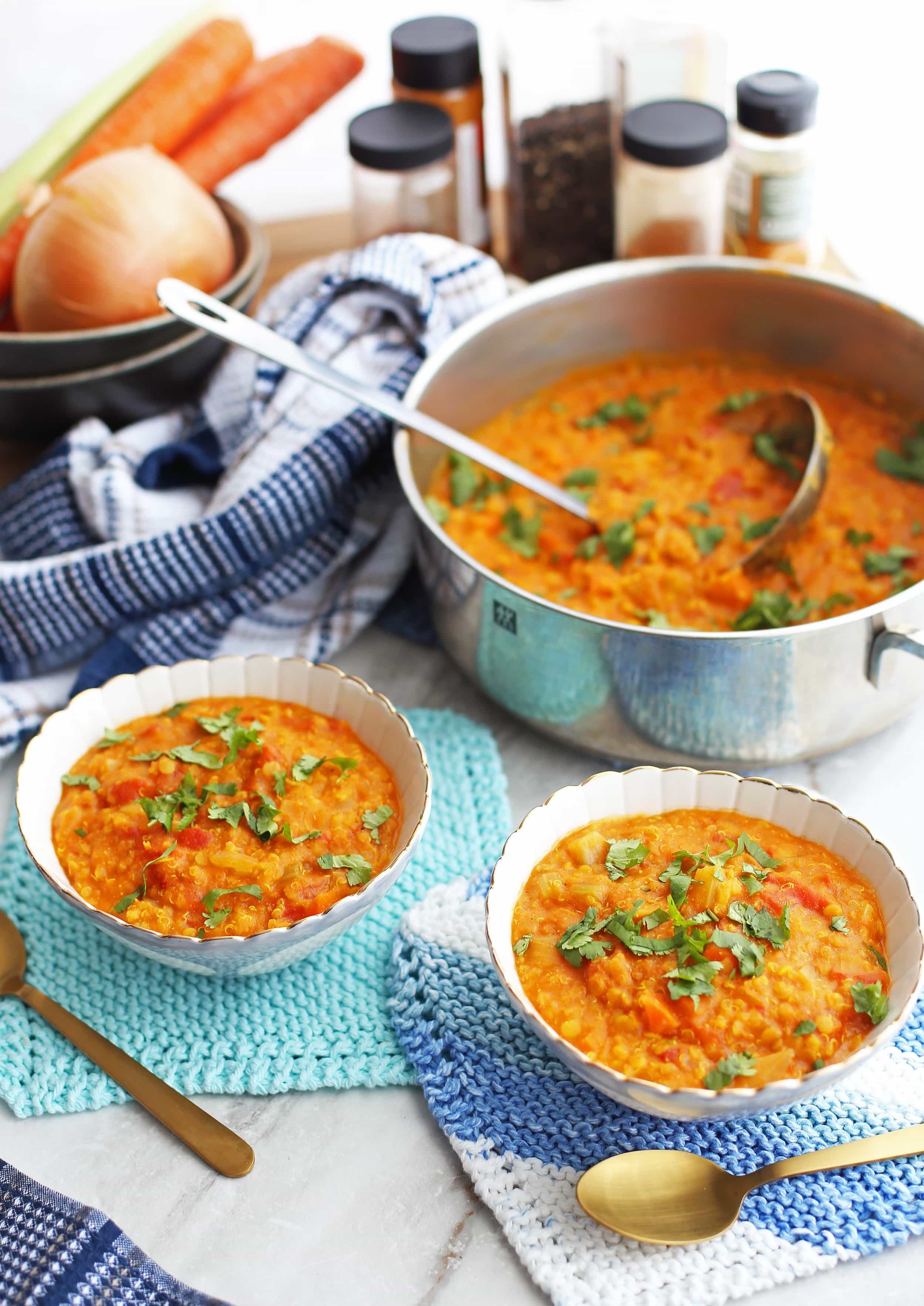 Two bowls of Curried Red Lentil and Quinoa Vegetable Soup with more soup in a large pot.