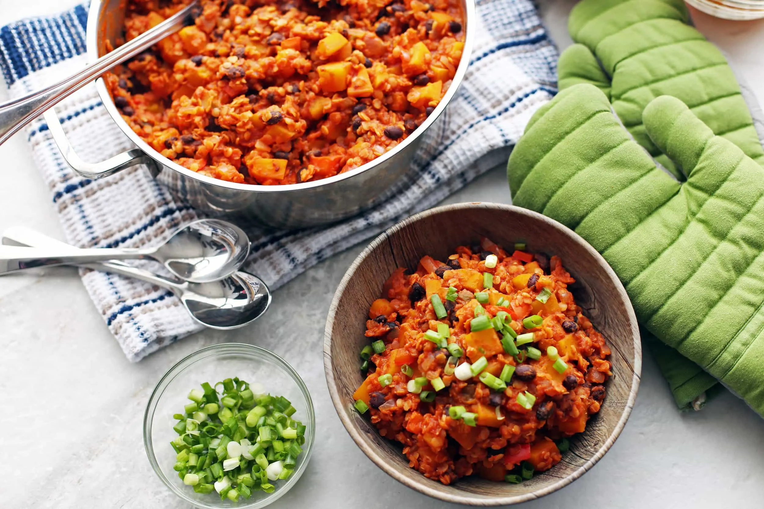 Overhead view of red lentil and butternut squash chili with green onions on top in a wooden bowl and in a pot.