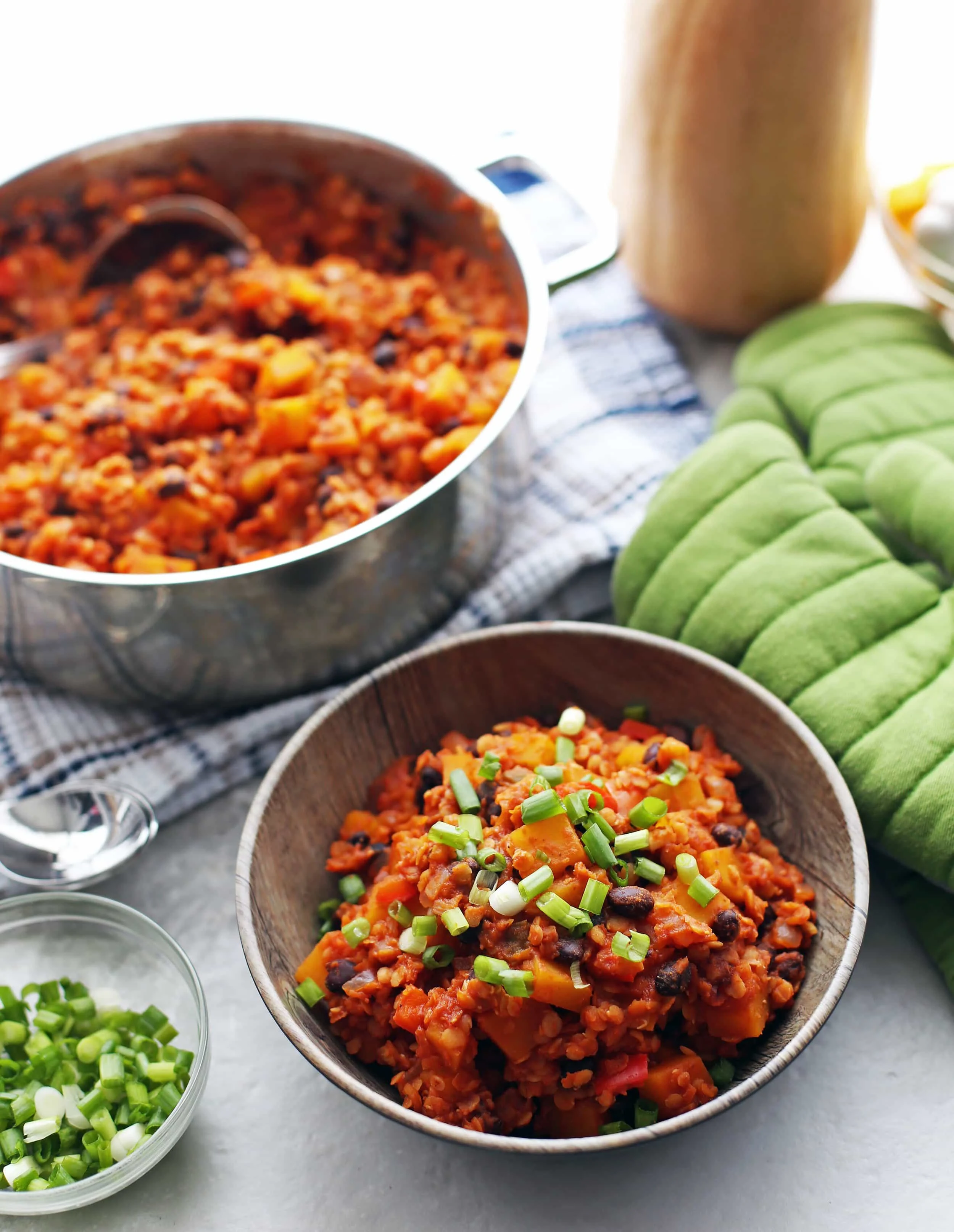 Red lentil butternut squash chili in a wooden bowl with chili in a pot in the background.