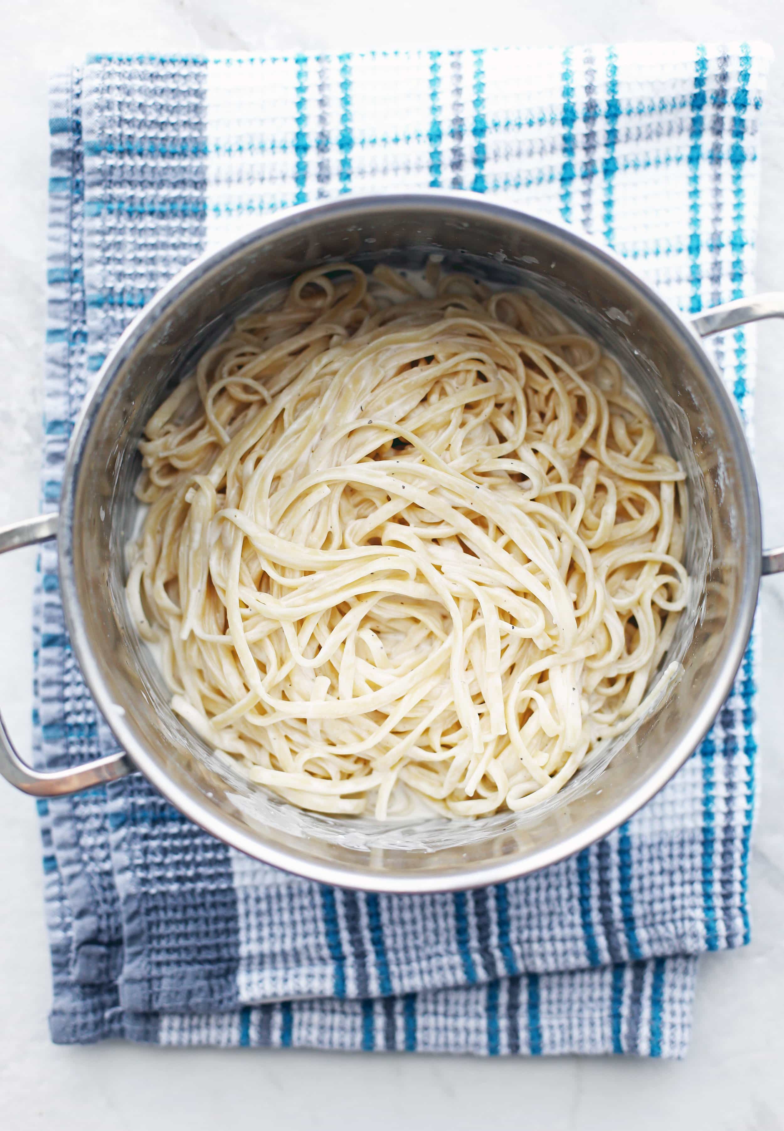 Al dente linguine pasta coated with creamy goat cheese sauce in a large metal pot.