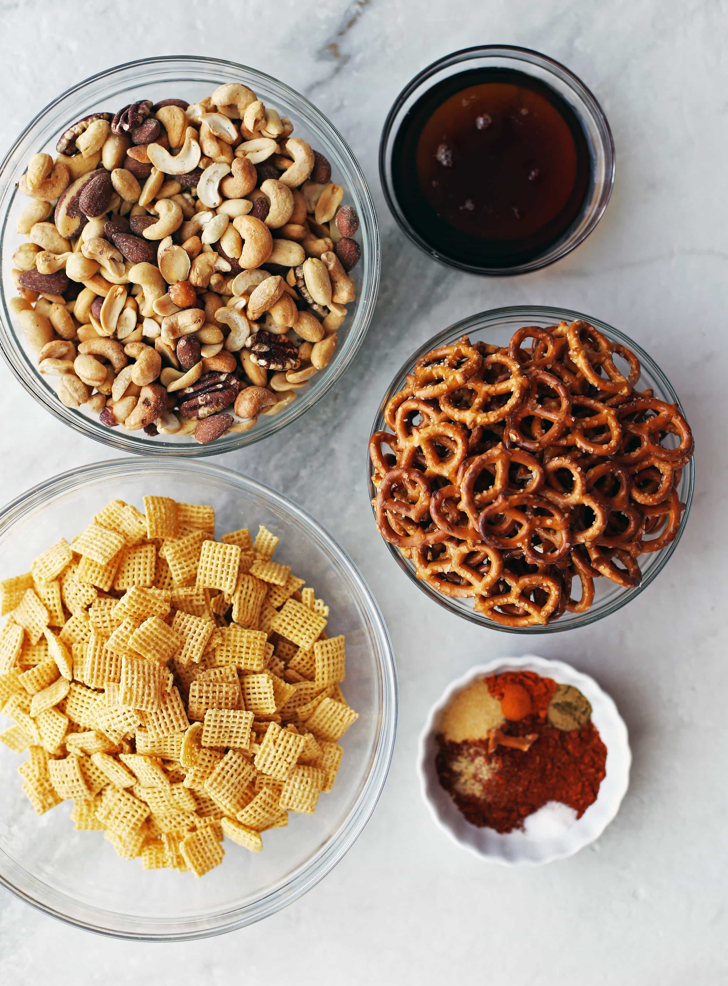 Glass bowls filled with Chex cereal, mini pretzels, mixed nuts, maple syrup, and spices.