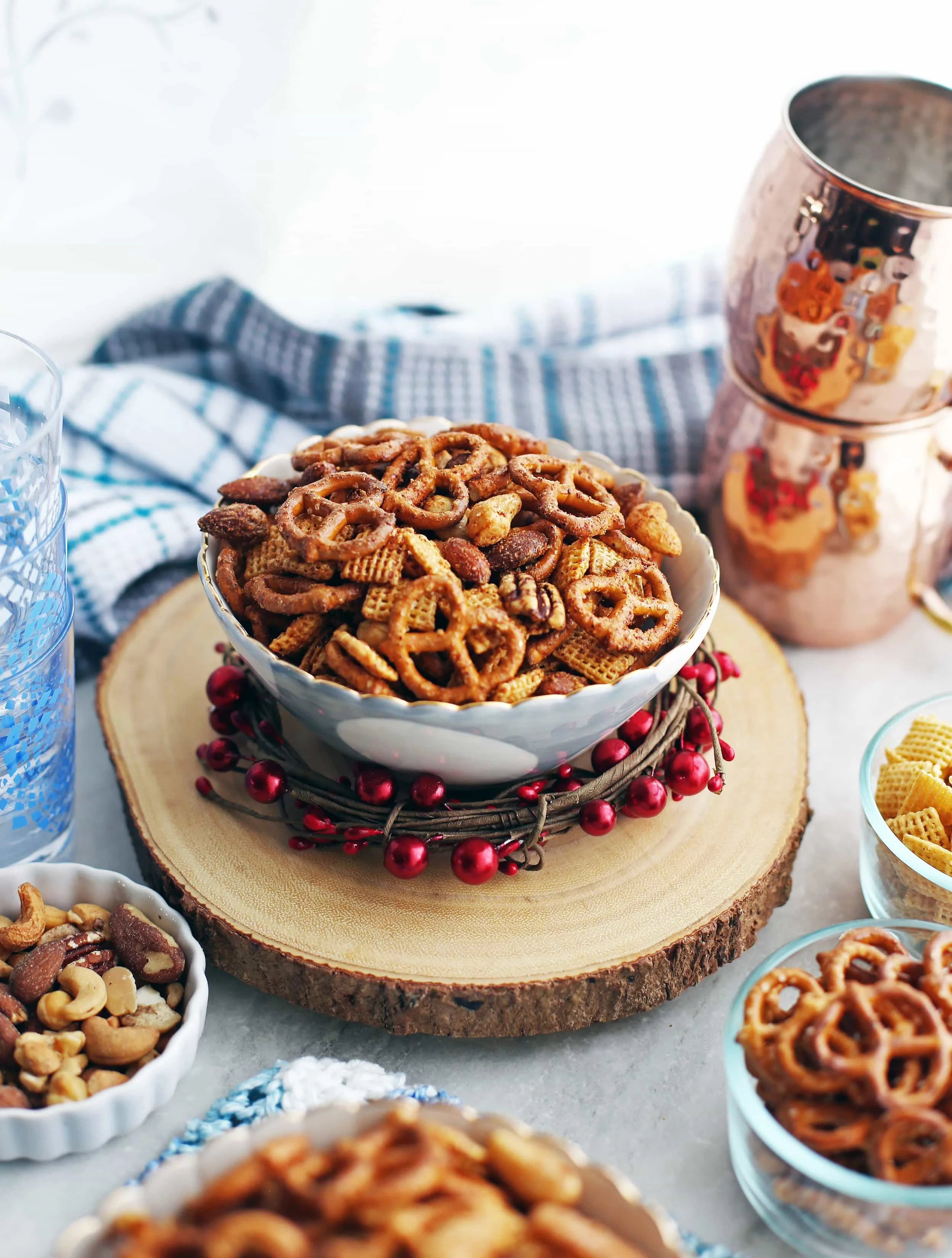 Side shot of a bowl of Maple Chili Nuts and Chex Mix with nuts, pretzels, and Chex cereal in the background.