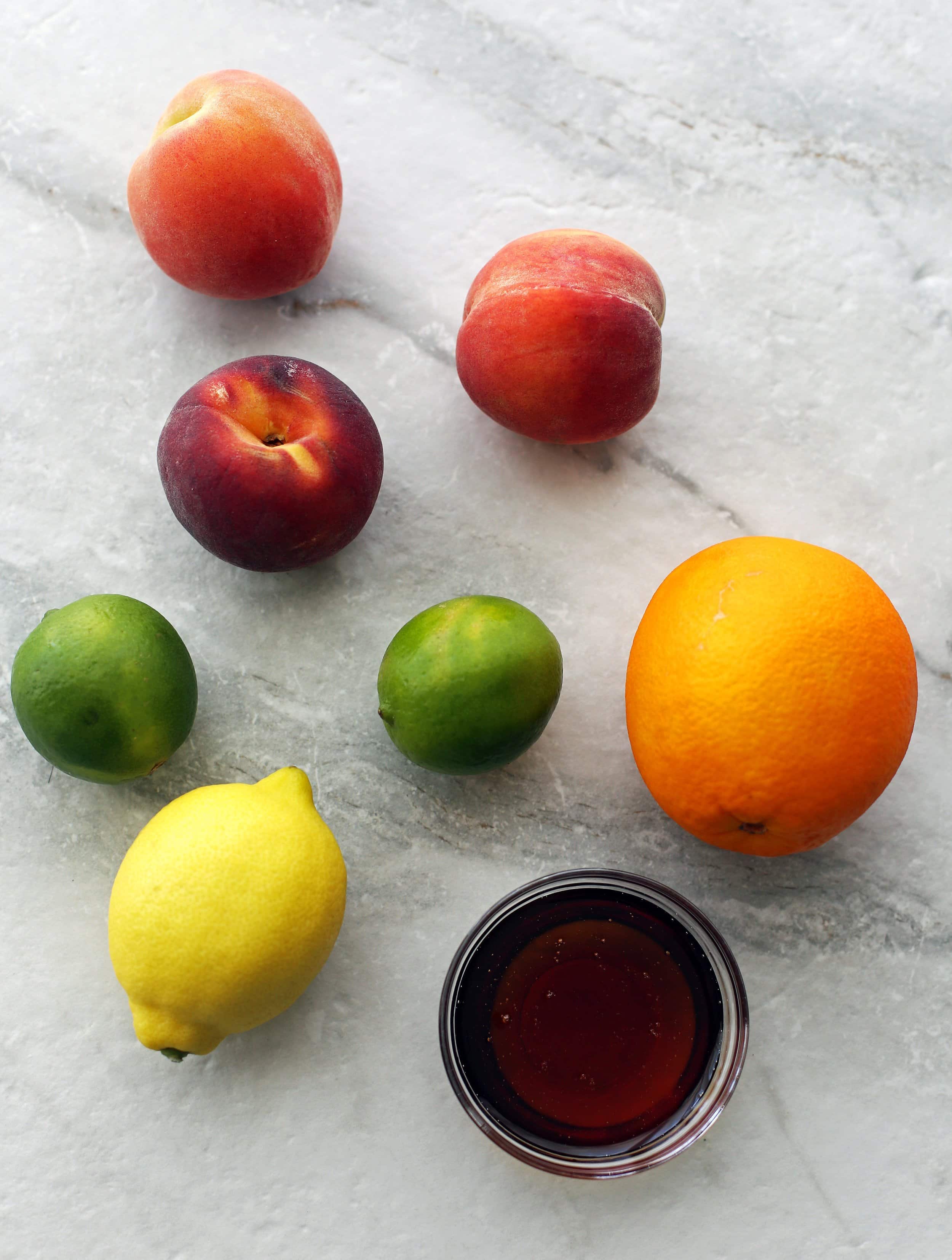 Three peaches, two limes, an orange, a lemon, and a bowl of maple syrup.