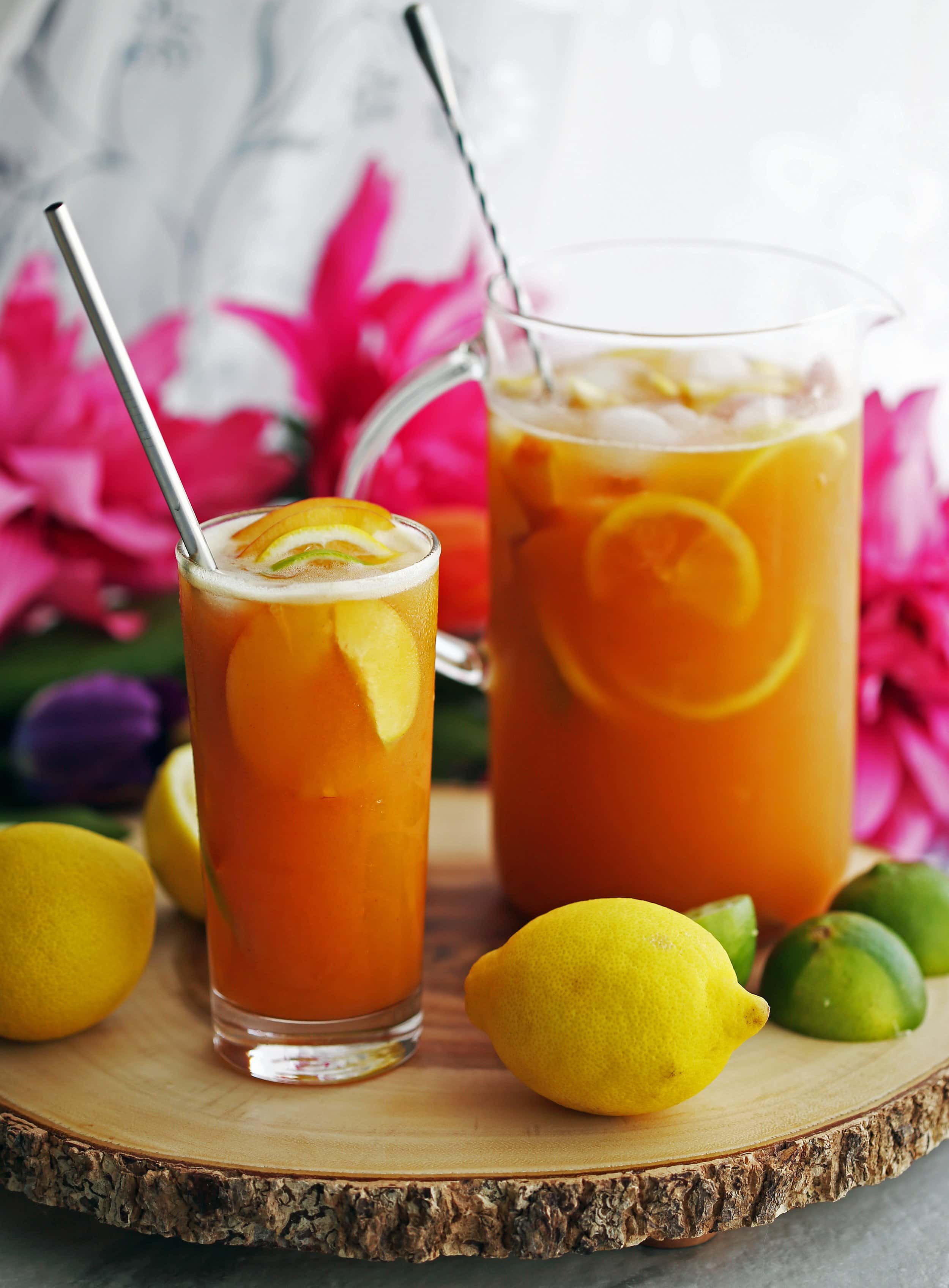 Maple peach citrus juice with fruit slices and ice in a tall drinking glass and glass container.