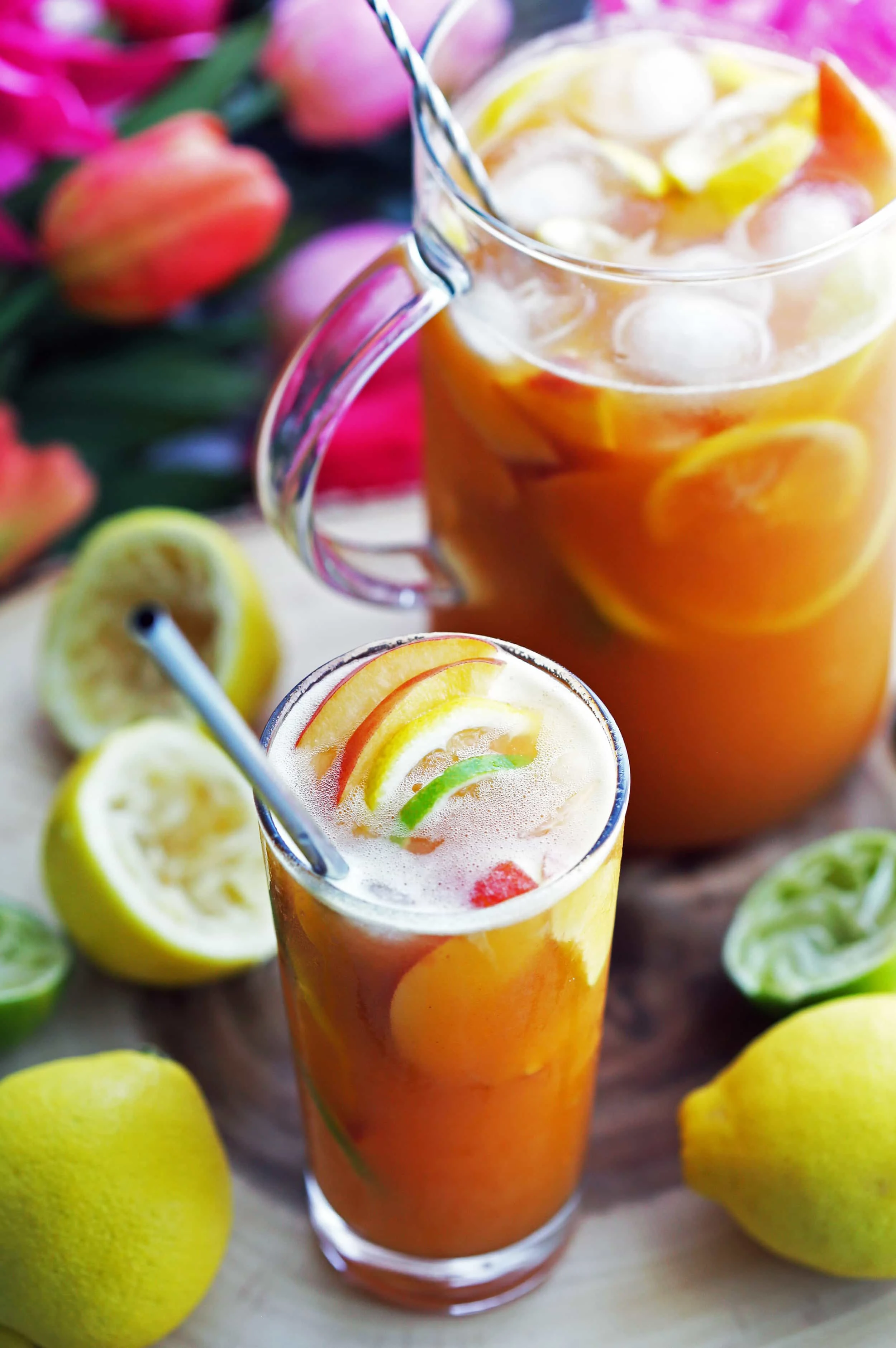 A close-up of a maple peach citrus juice with ice, fruit slices, and a straw in a tall drinking glass.