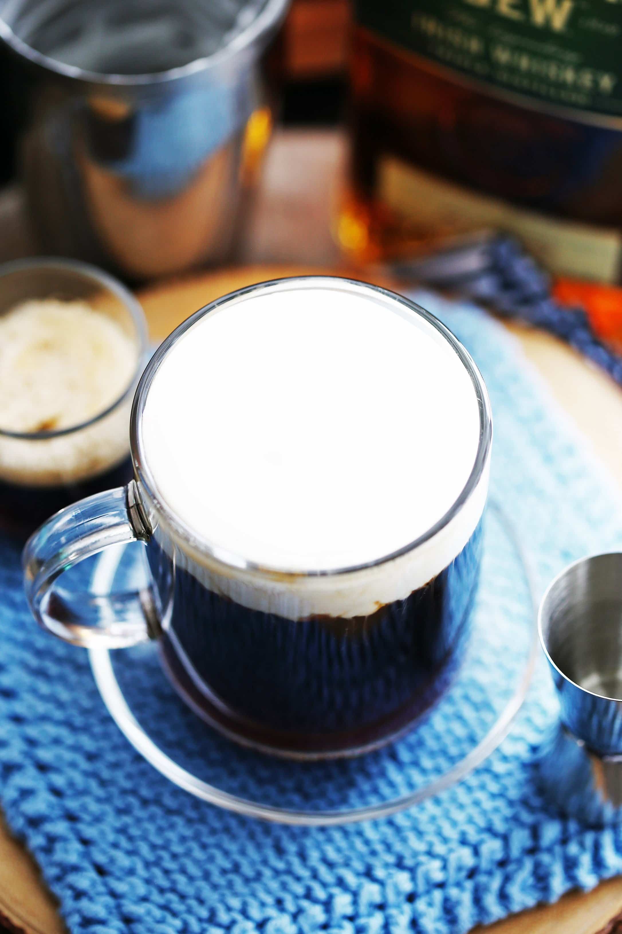 An Irish coffee cocktail sweetened with maple syrup and topped with lightly whipped cream in a glass mug.