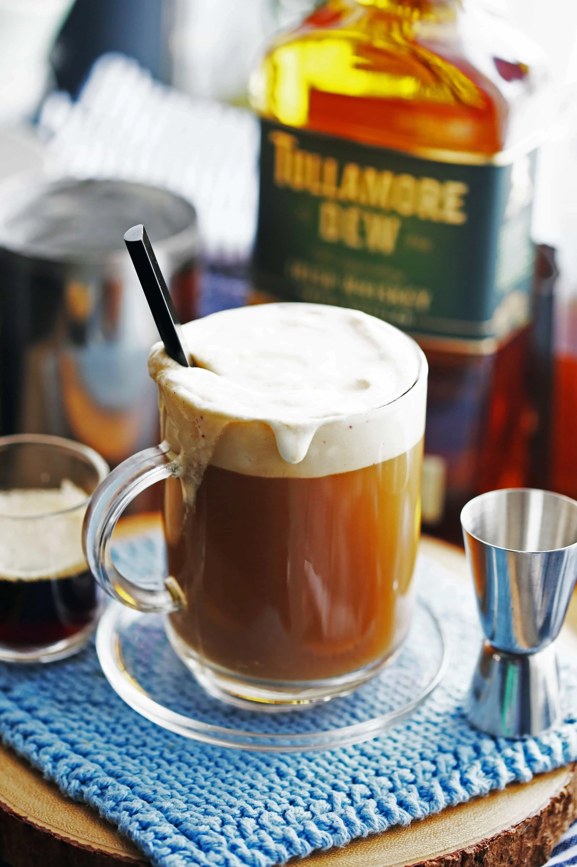 A glass mug filled with Maple Irish Coffee, gently stirred, with a black stirring spoon in it.