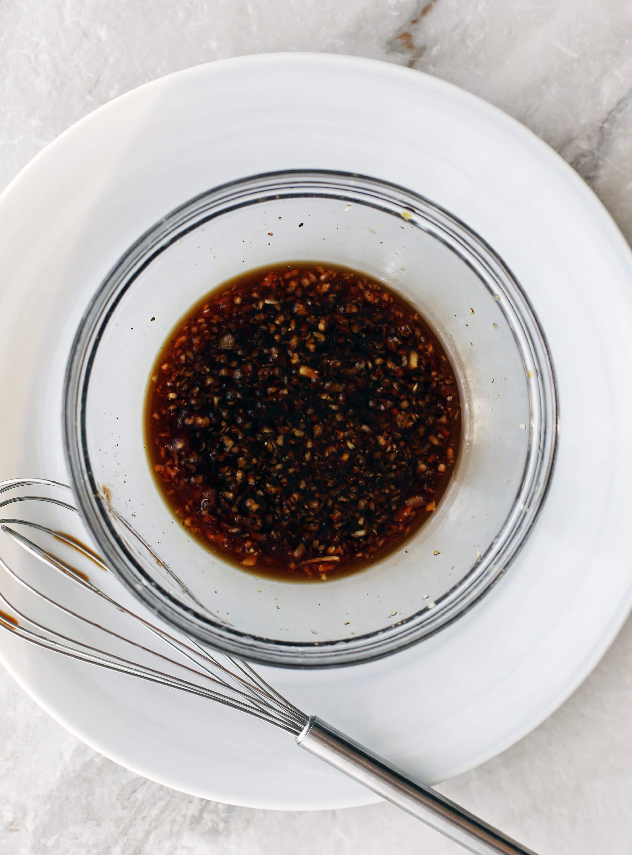 A clear bowl containing maple syrup, soy sauce, garlic, ginger, salt, and pepper.