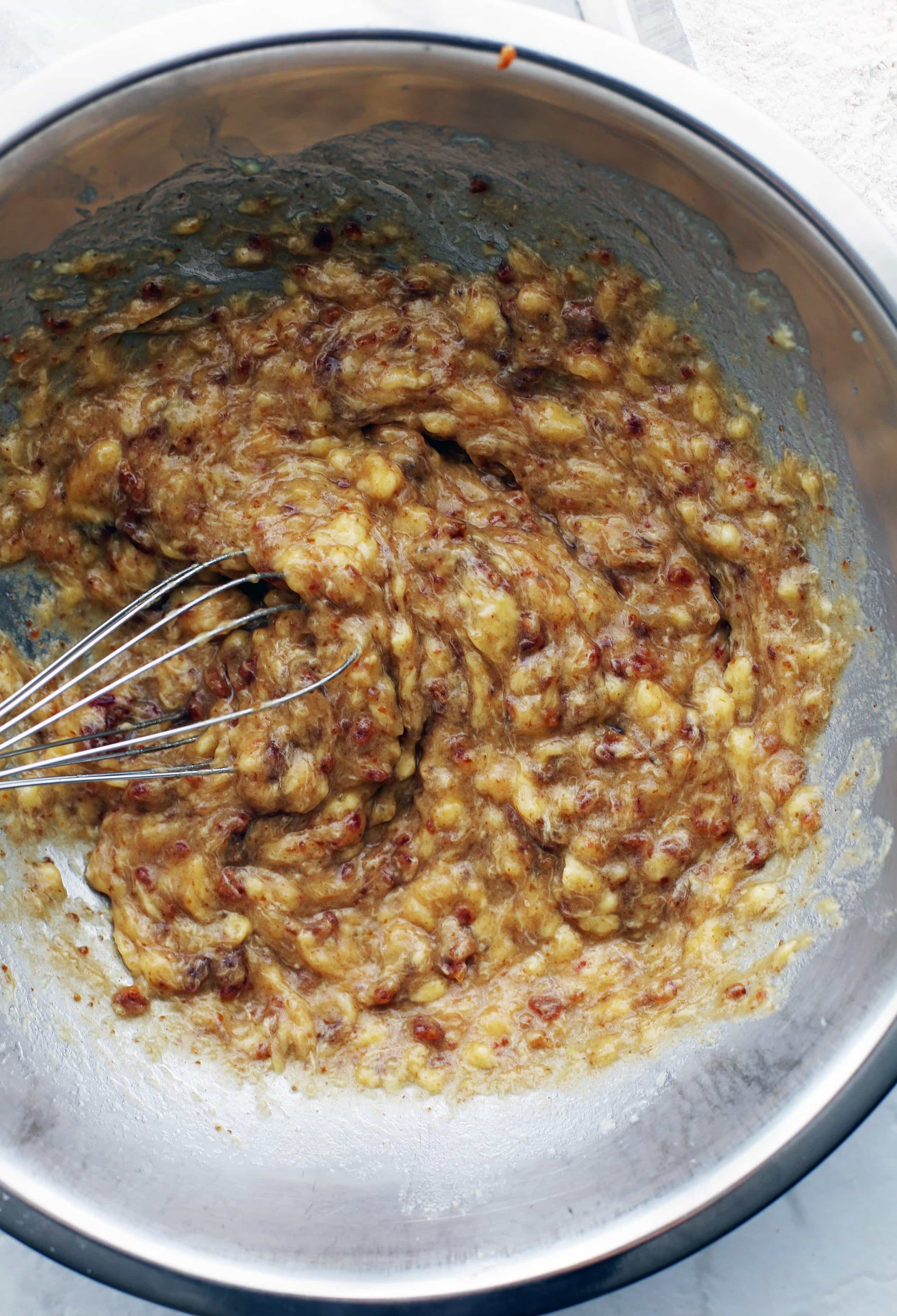 Medjool date paste, mashed bananas, and hot water mixed together using a wire whisk in a metal bowl.