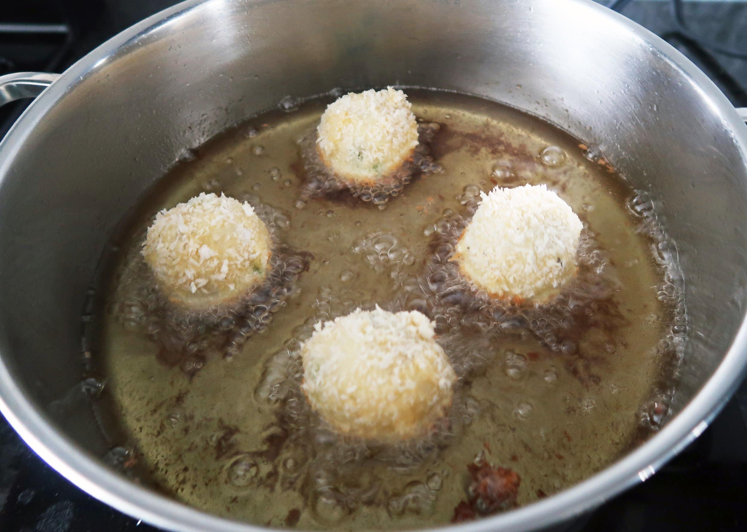 Four potato balls frying in a pot of oil.