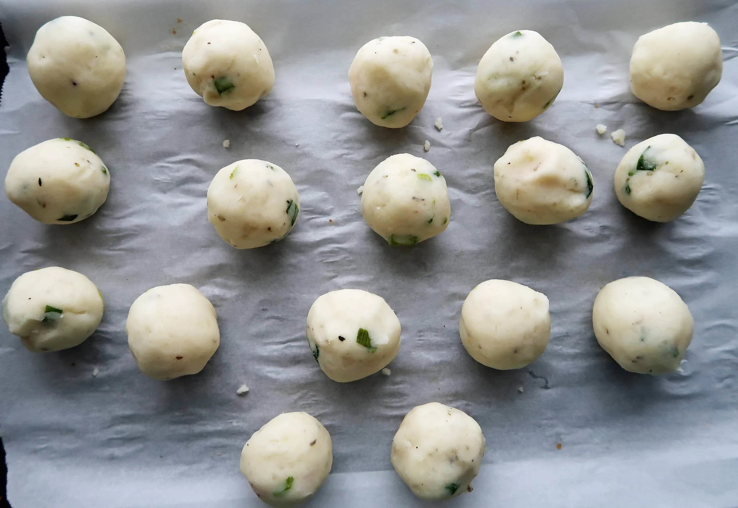 Balls of mashed potato on a baking sheet.