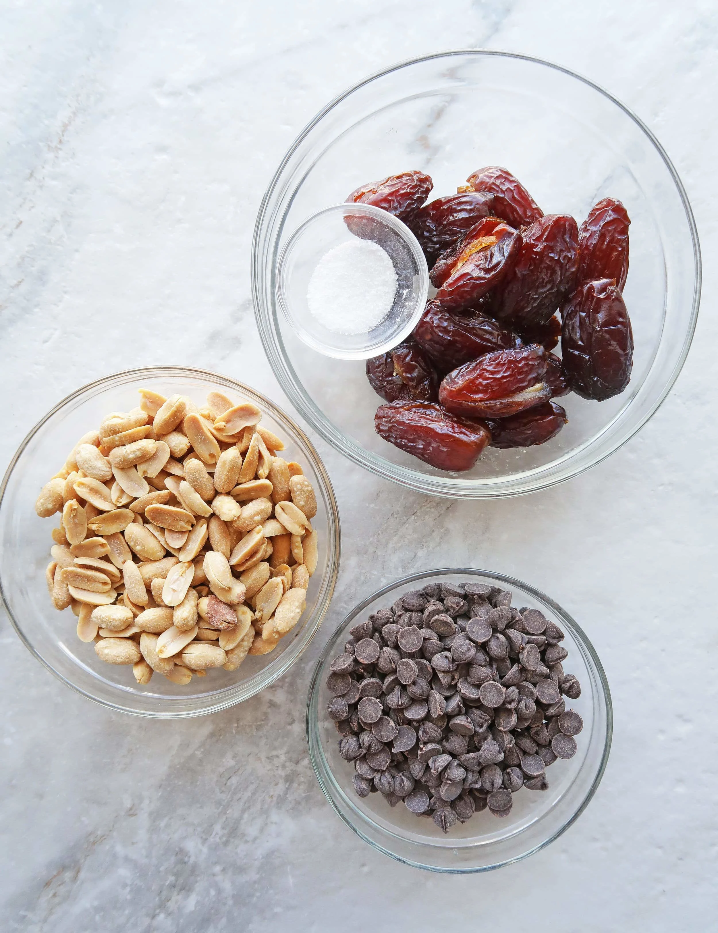 Bowls of roasted salted peanuts, chocolate chips, Medjool dates, and salt.