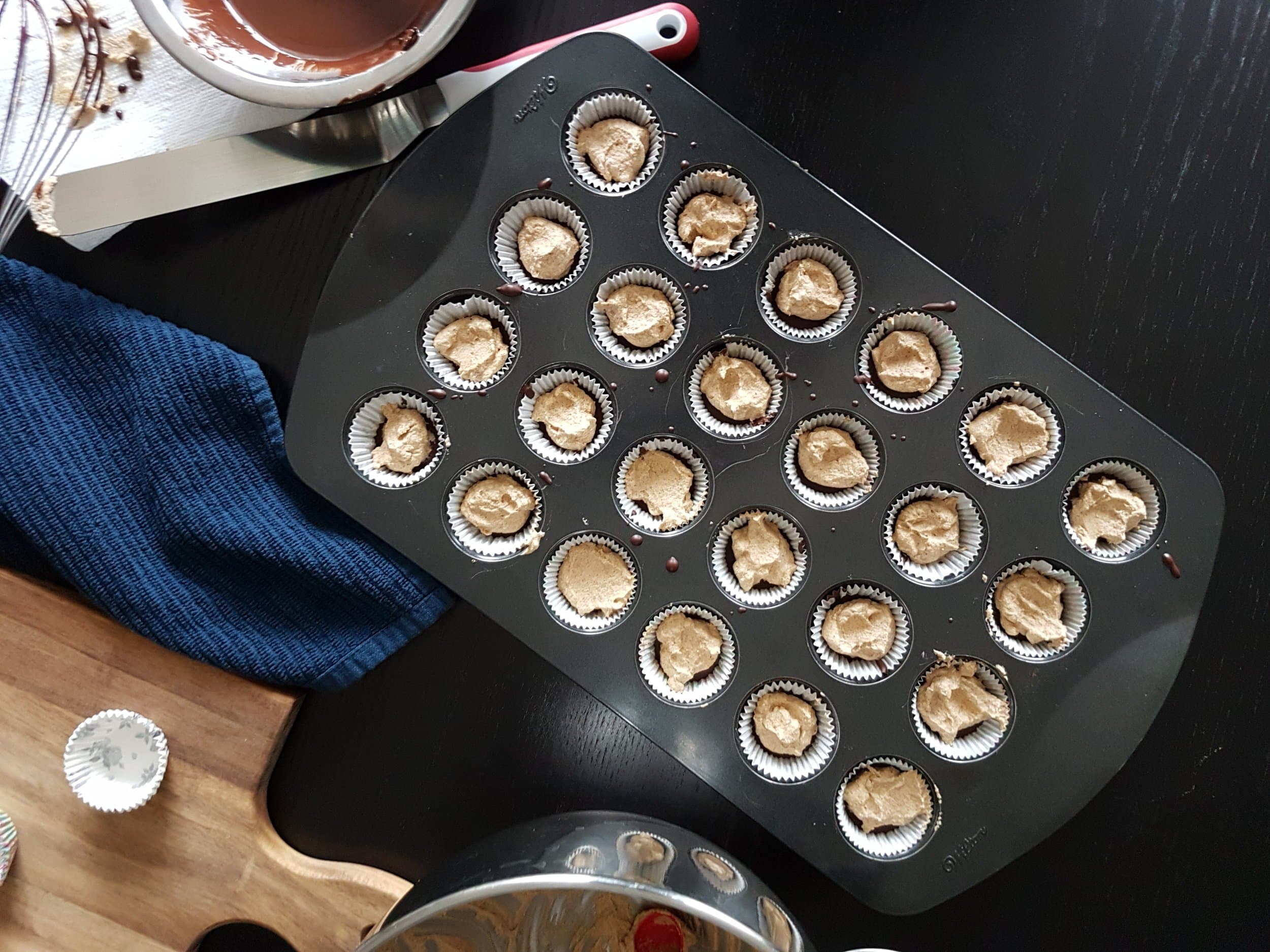 Mini chocolate cups in a pan being filled with pumpkin spice whipped cream.