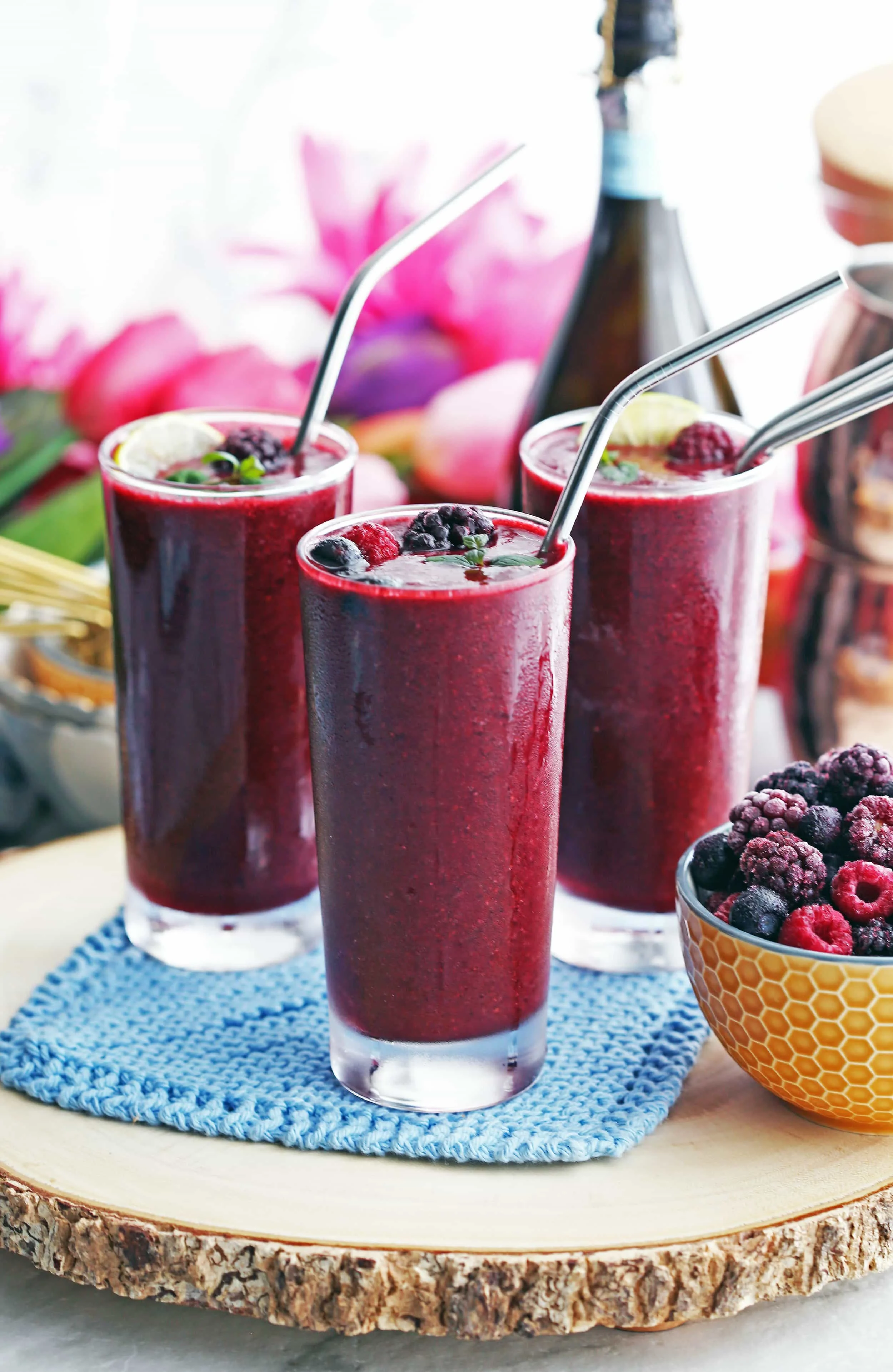 Three tall glasses of Mixed Berry Prosecco Wine Slushies with straws and berry garnish. A bowl of frozen berries beside them.