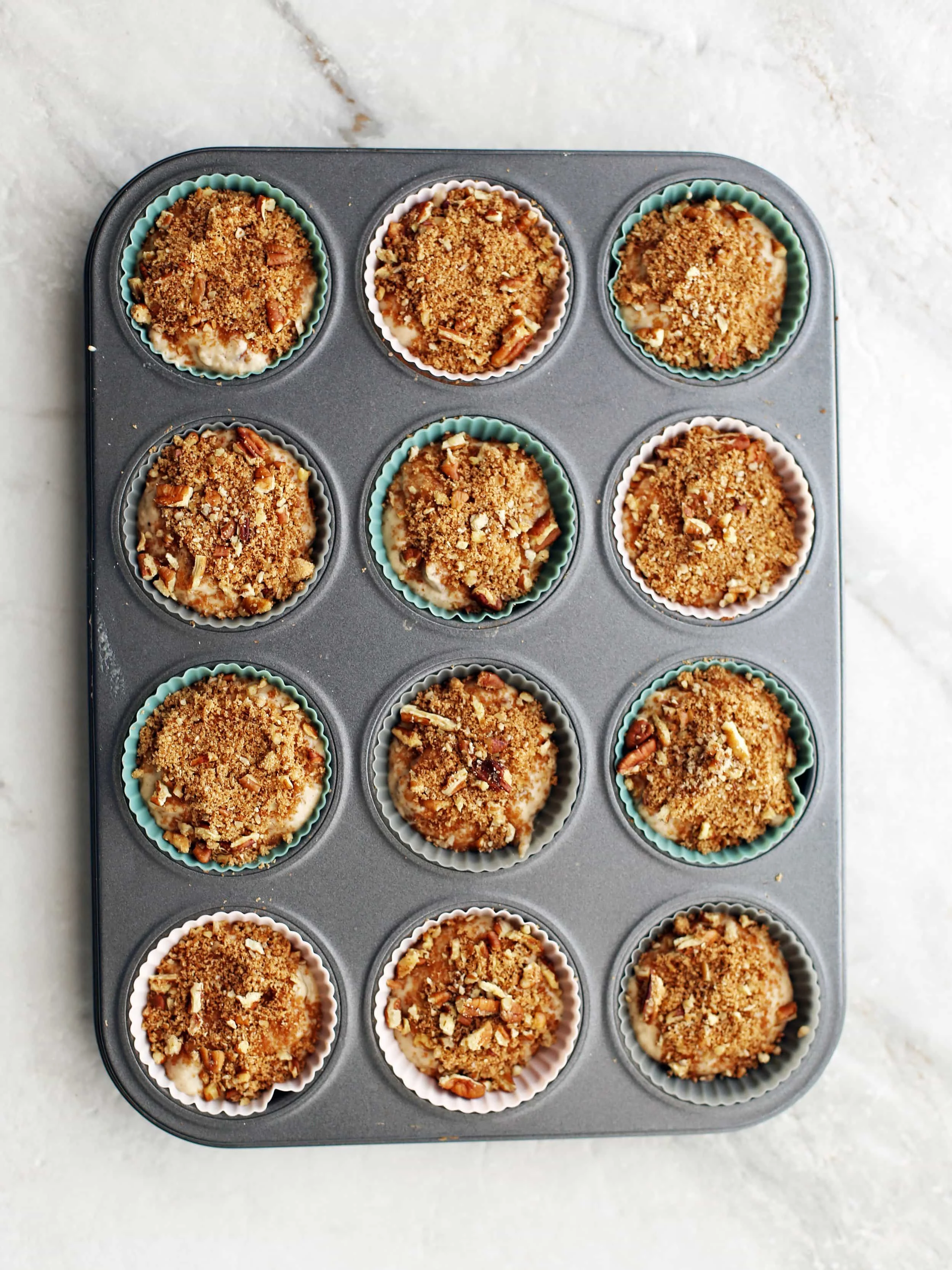 Pre-baked cinnamon pecan applesauce muffins in a muffin baking pan.