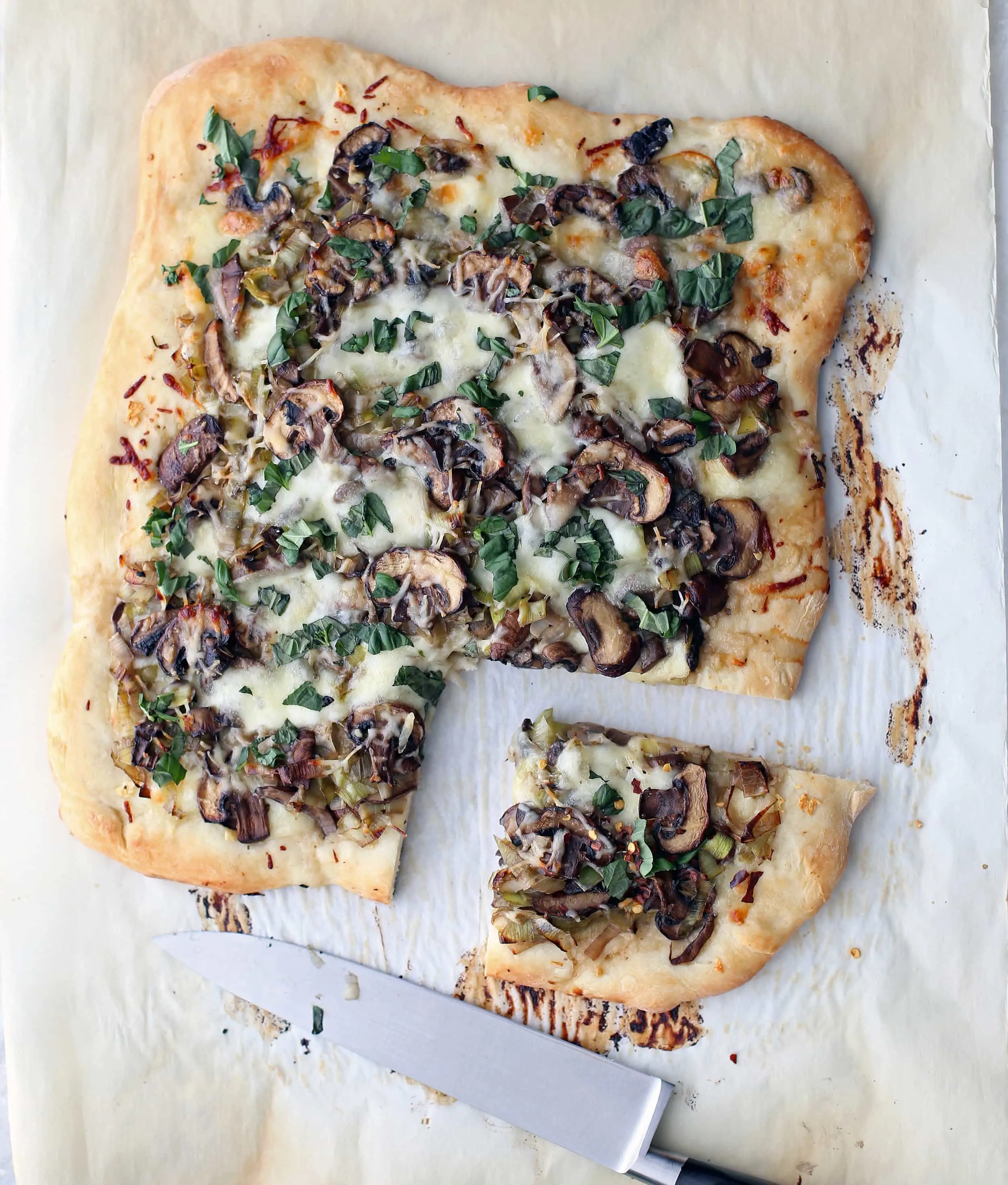 Baked leek mushroom mozzarella pizza with one slice cut on parchment paper.