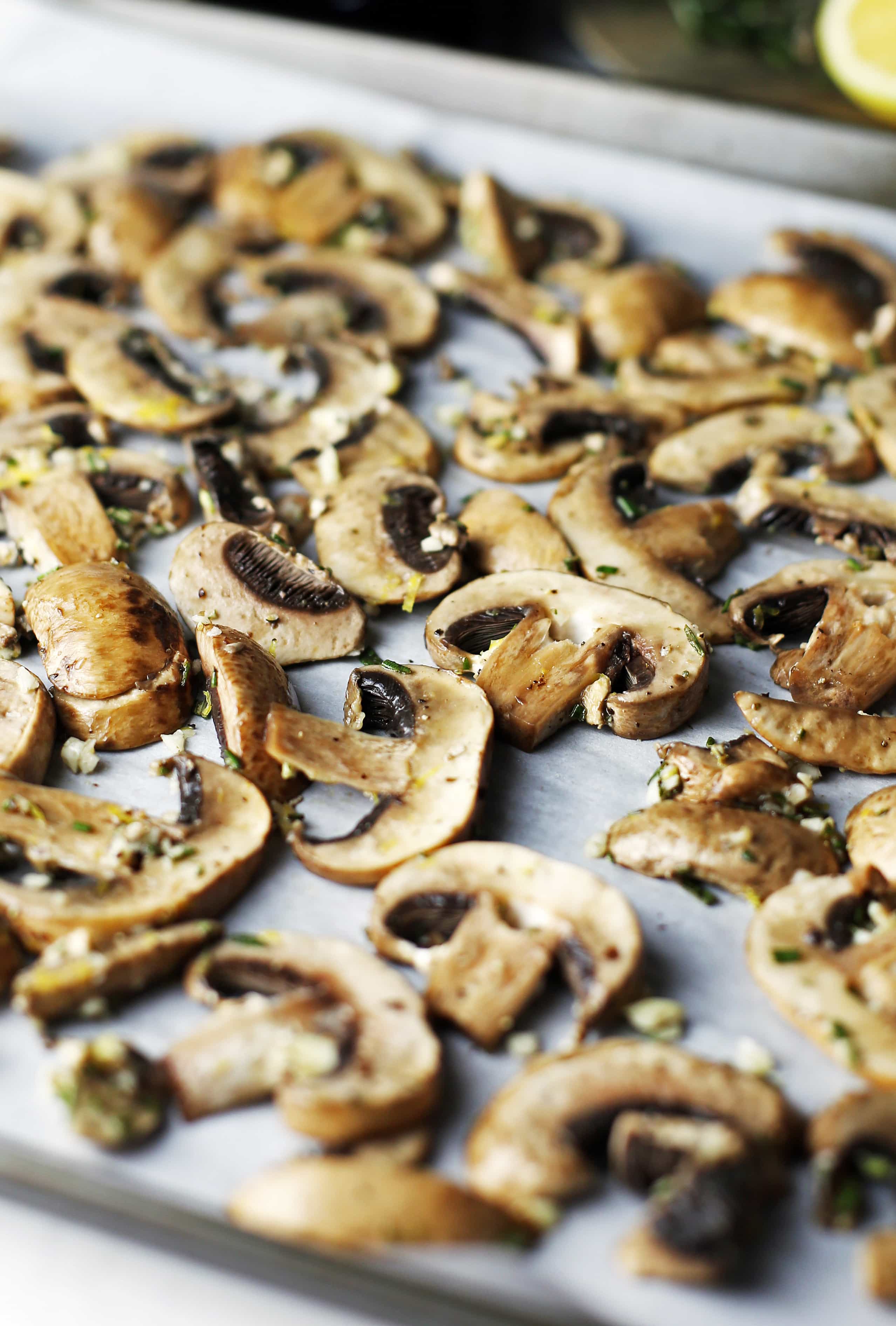 Sliced mushrooms with rosemary and garlic spread on a baking sheet.