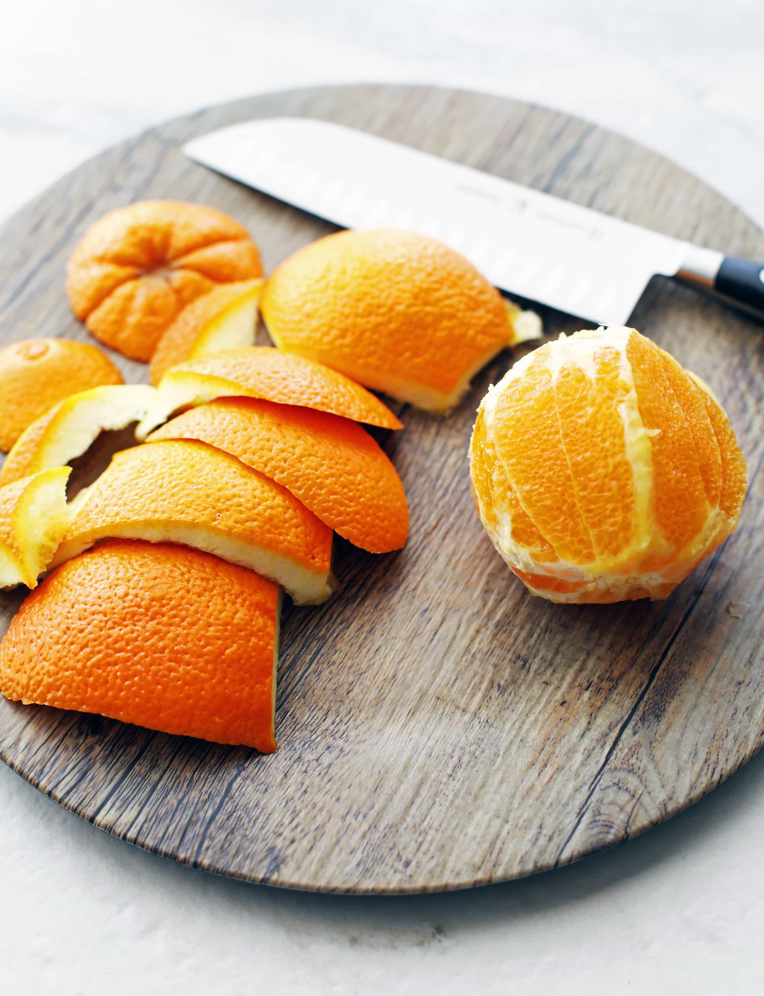 A cut and peeled navel orange and a large knife on a wooden platter.