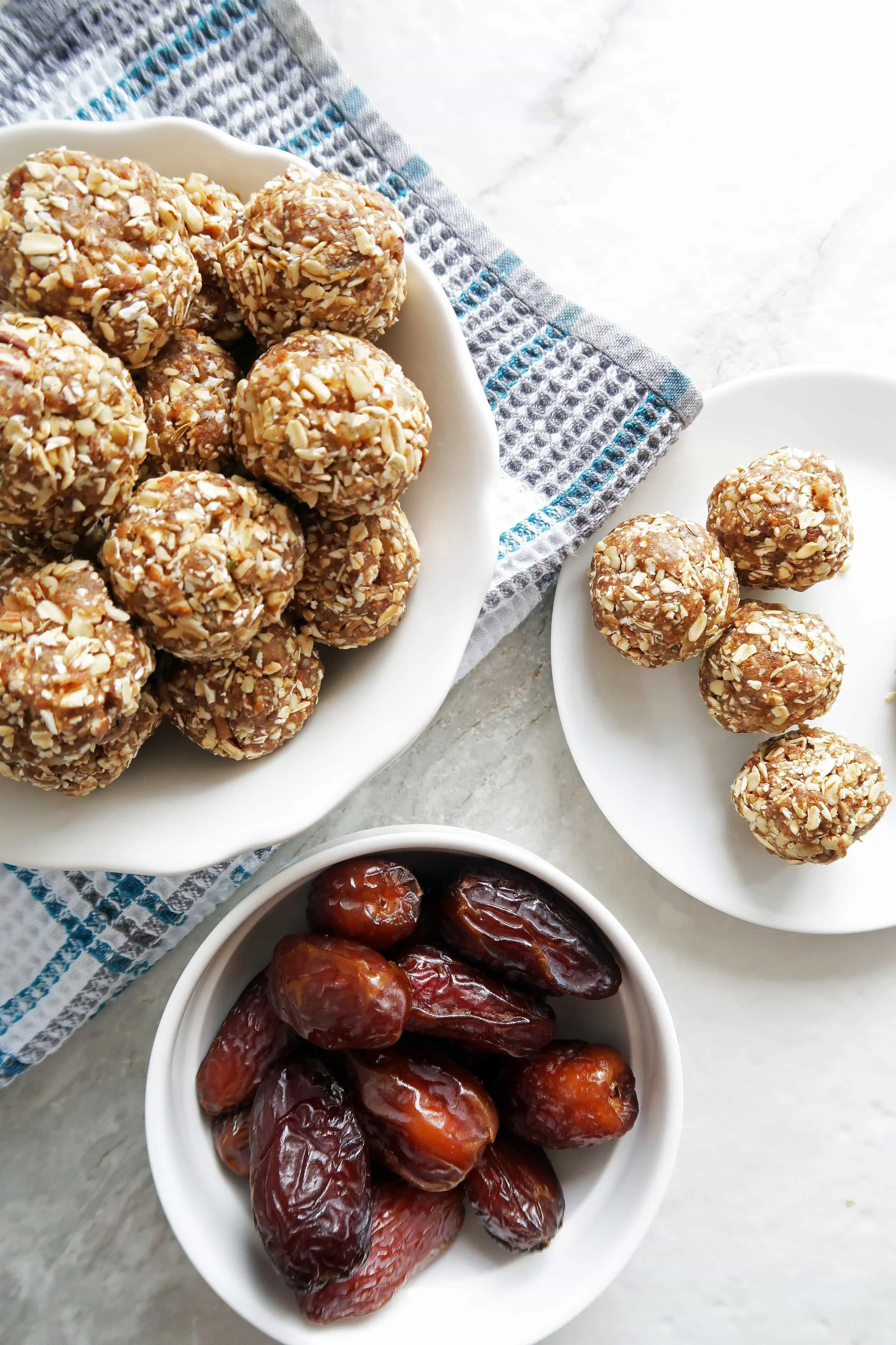 No Bake Chai Spiced Date Energy Balls pilled in a white bowl, energy balls on a white plate, and a bowl of dates to its side.